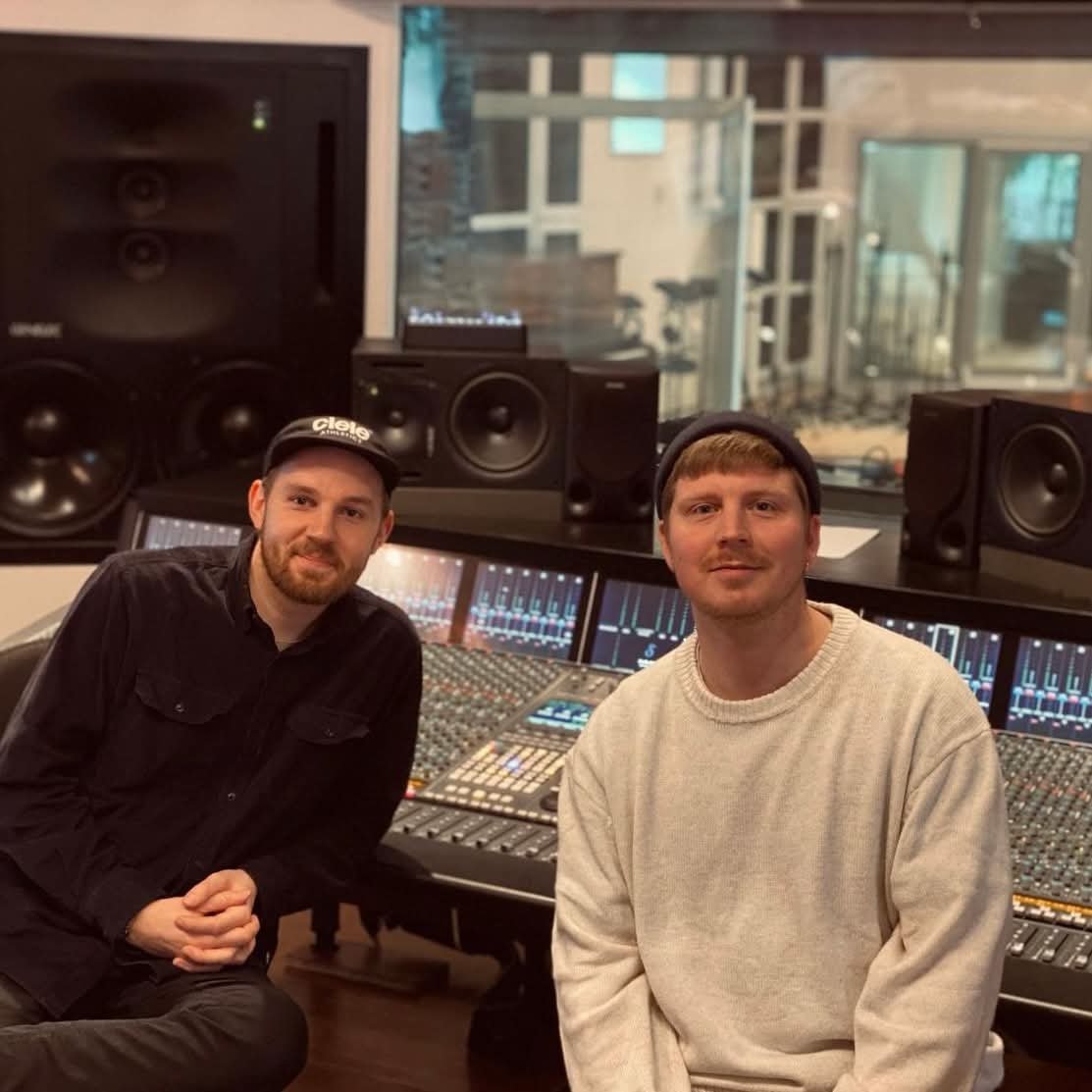 To unge mænd sidder foran en stor lydmixer i et musikstudie, omgivet af professionelle højttalere | Musikkomposition | Studieproduktion | Mixbiograf | Filmproduktion Aarhus | GESTALT