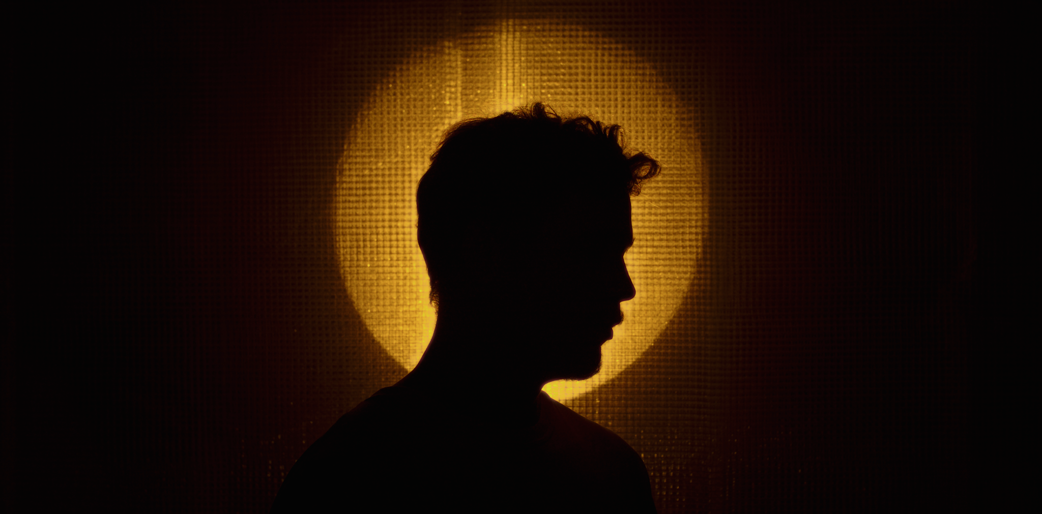 Silhuet af person med profil mod en gul-garvet baggrund og en stor cirkel lys bagved | Kortfilm | Wild Wild Vesløs | Esben Persson | Filmproduktion Aarhus | GESTALT