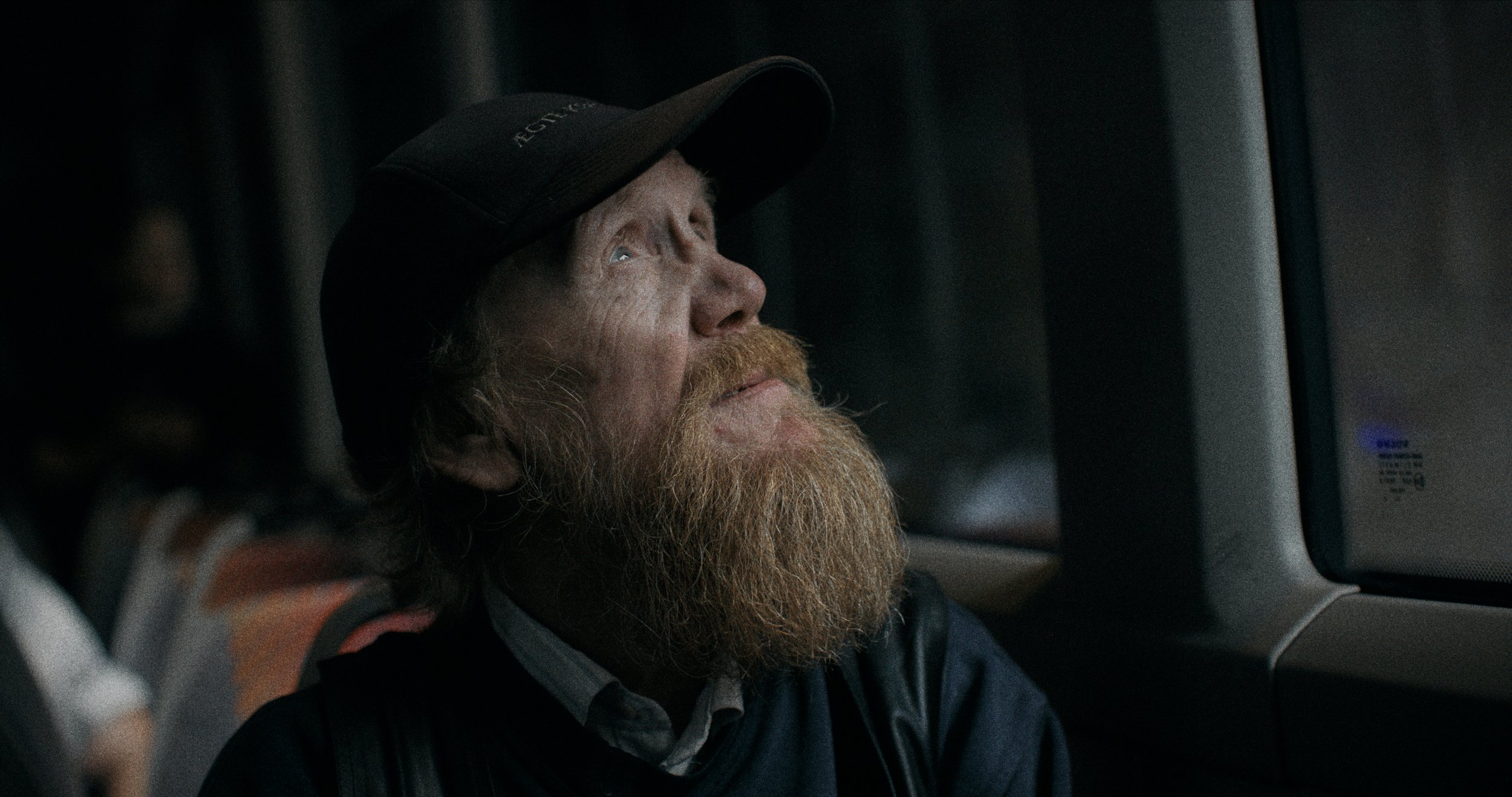 En mand med rødskæg og hat ser ud gennem et vindue, mens han sidder på et transportmiddel | Dokumentarfilm | Retrograd | Esben Persson & Anders Mielcke  | Filmproduktion Aarhus | GESTALT
