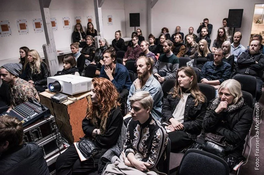 En gruppe mennesker sidder i et industrielt biografrum og ser opmærksomt mod lærredet | Film- og fotofestival på Aarhus Kunstakademi ved navn Aarhus Independent Pixels | Eventbilleder | Filmproduktion Aarhus | GESTALT