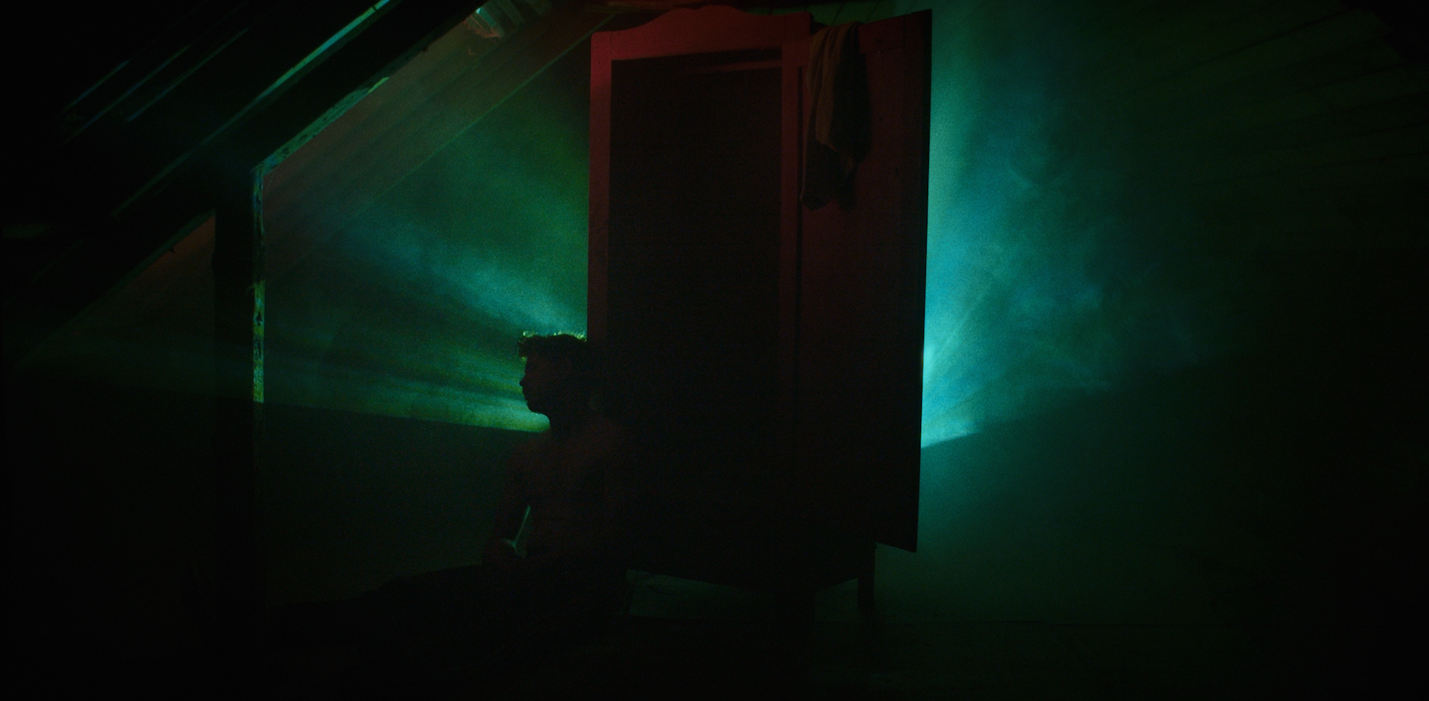 Person sidder foran et åbent skab, med en grøn lysstråle bagved, på et mørkt værelse.
