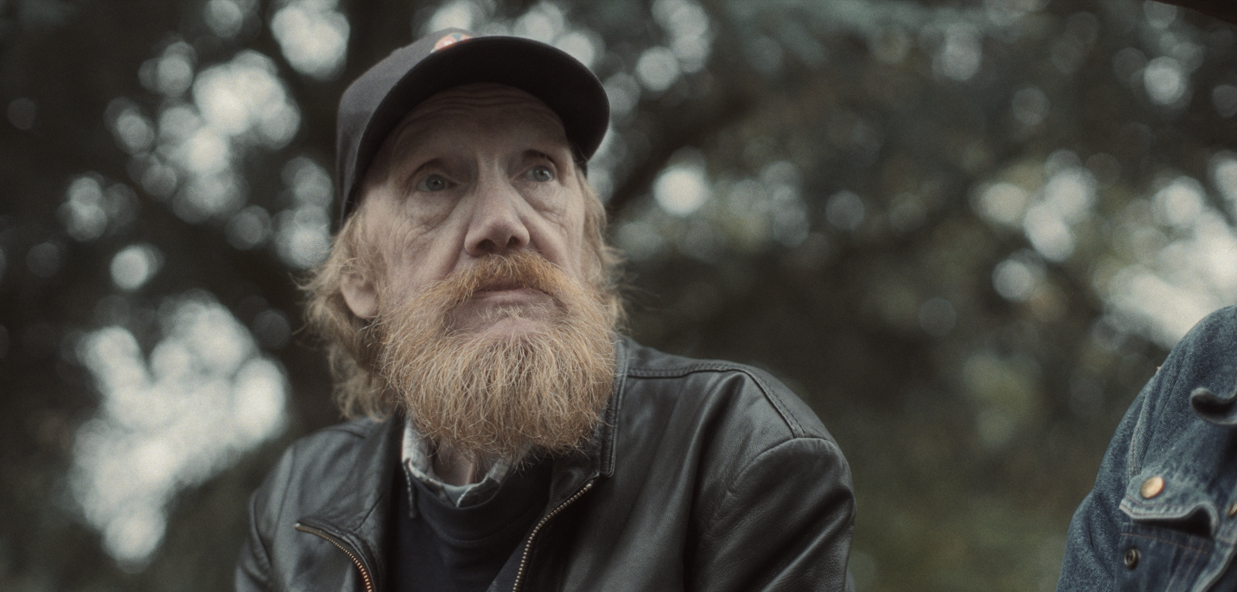 En mand med rødt skæg, rødt hår og en sort læderjakke, ser tænksom ud i udendørs omgivelser | Dokumentarfilm | Retrograd | Esben Persson & Anders Mielcke | Filmproduktion Aarhus | GESTALT