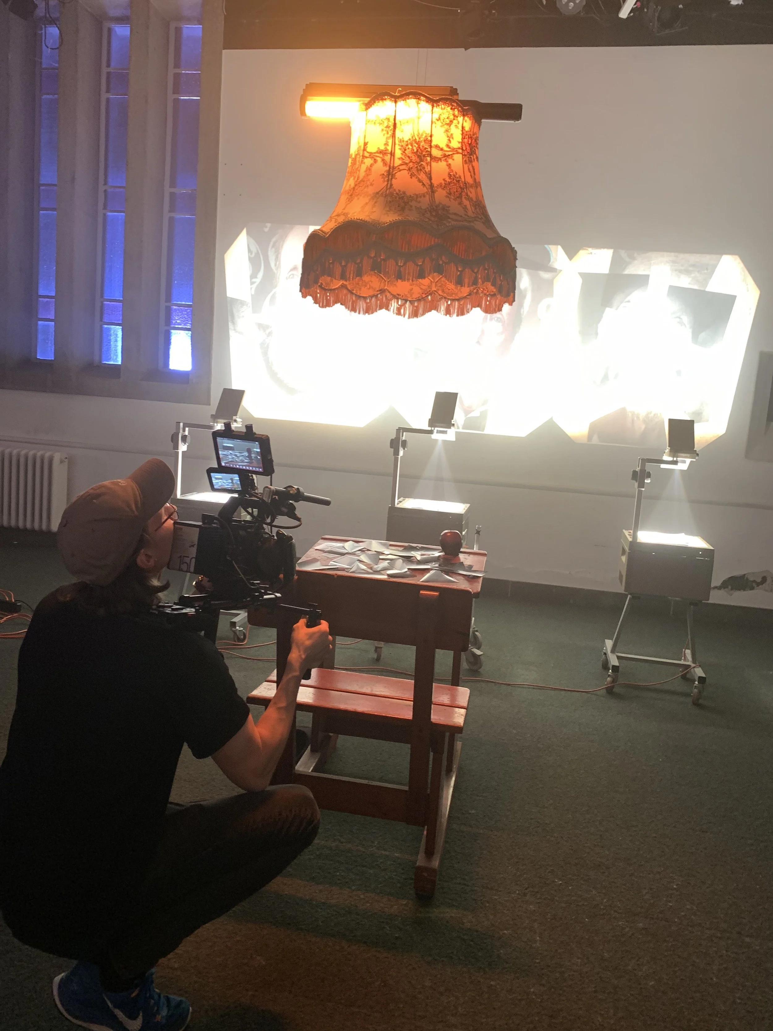 En person, der arbejder med kamera, peger mod en væg med en projektion af en vintage lampeskjuler. Der er tre muligheder projektorer foran væggen | Dokumentarfilm | Retrograd | Esben Persson & Anders Mielcke | Filmproduktion Aarhus | GESTALT