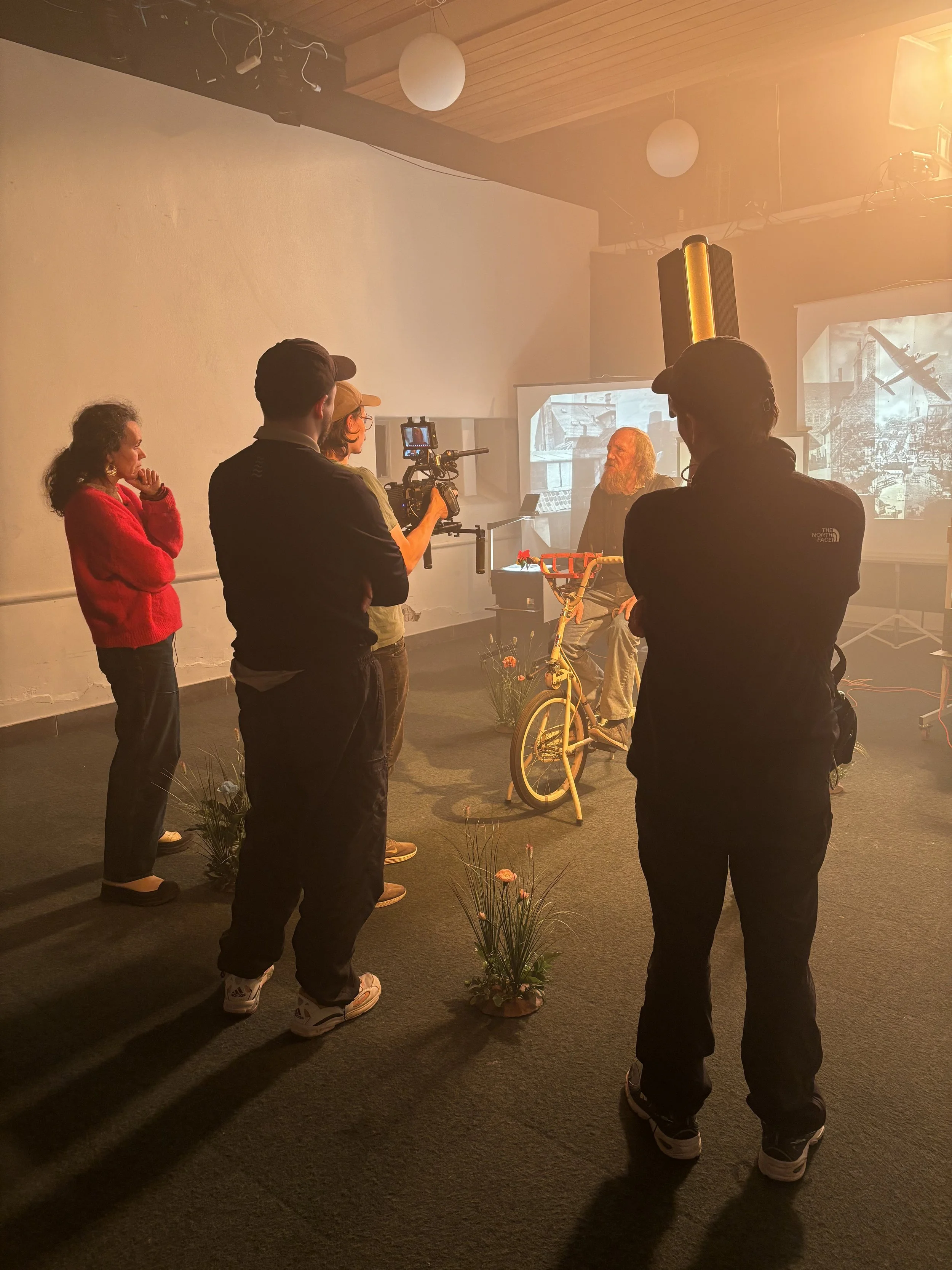 En filmproduktion med flere personer, der arbejder på en scene, hvor en ældre mand med langt skæg sidder på en motionscykel | Dokumentarfilm | Retrograd | Esben Persson & Anders Mielcke | Filmproduktion Aarhus | GESTALT