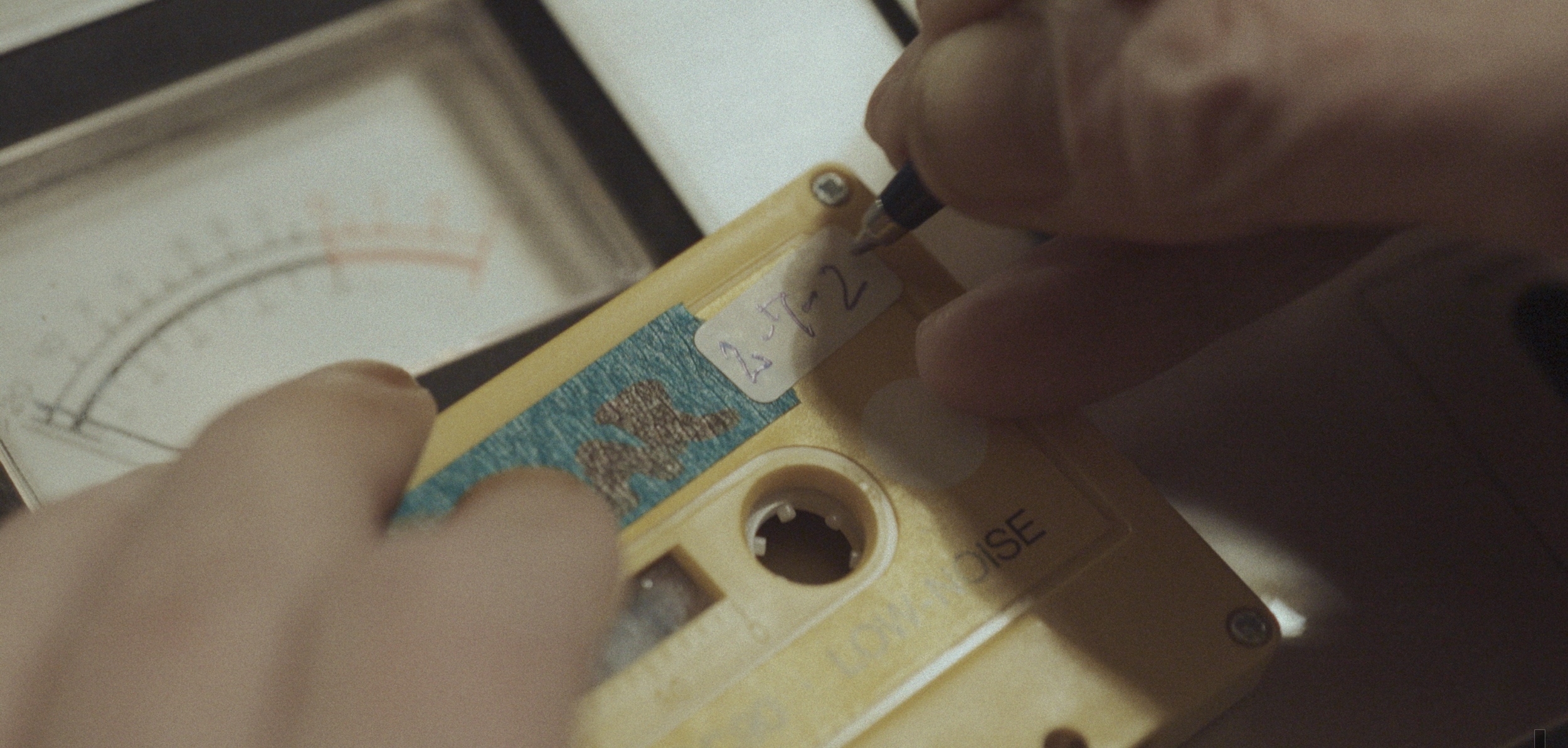 En person skriver med en sort pen på et kassettebånd | Dokumentarfilm | Retrograd | Esben Persson & Anders Mielcke | Filmproduktion Aarhus | GESTALT
