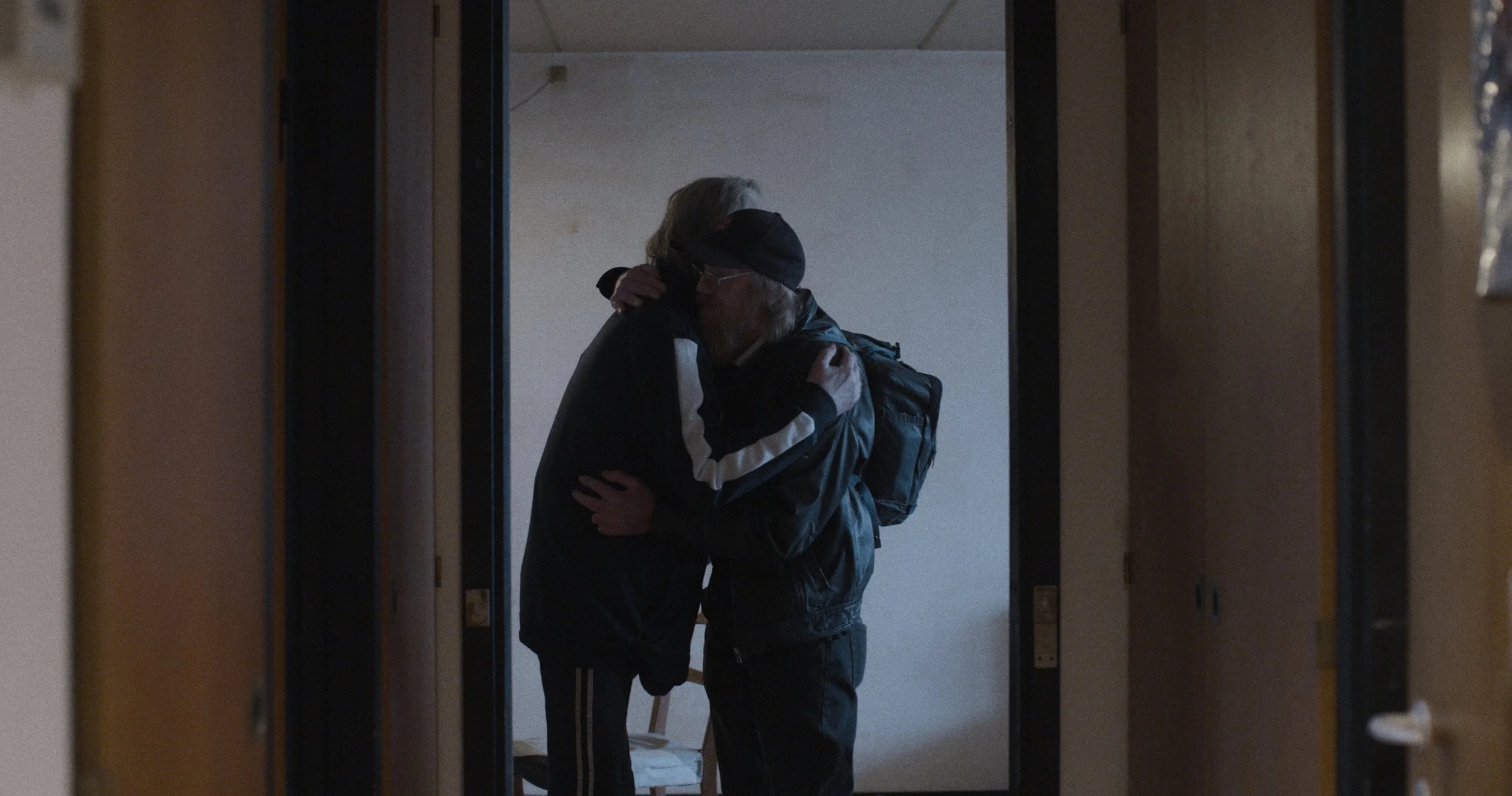 To personer, der krammer hinanden i en gang, set gennem en åben dør | Dokumentarfilm | Retrograd | Esben Persson & Anders Mielcke | Filmproduktion Aarhus | GESTALT