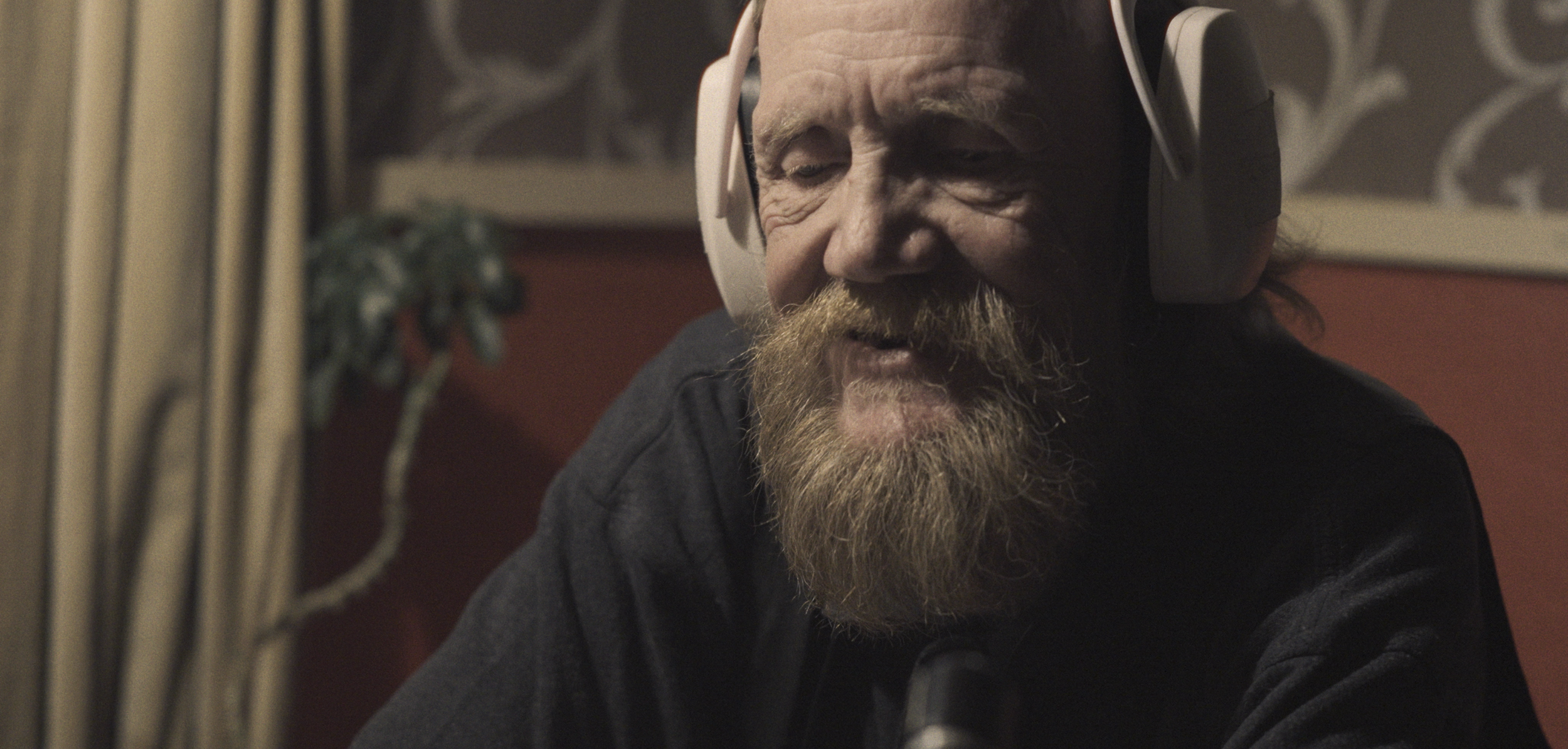 En ældre mand med skæg, der har høretelefoner på, smiler og snakker | Dokumentarfilm | Retrograd | Esben Persson & Anders Mielcke | Filmproduktion Aarhus | GESTALT