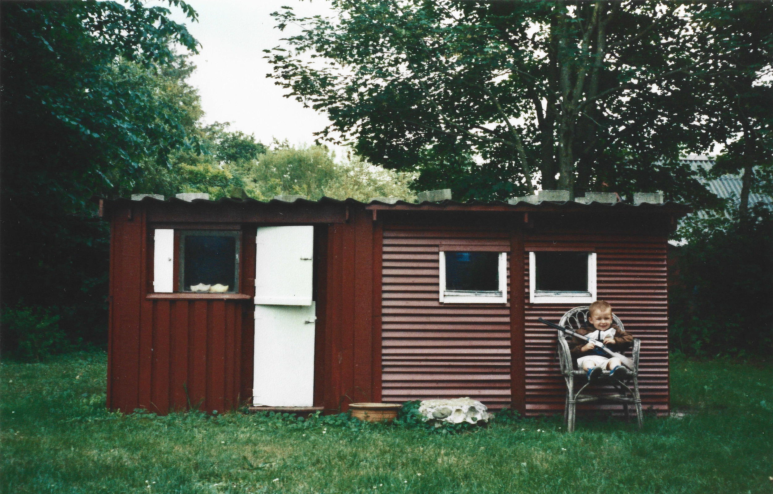 En glad dreng i en stol foran hytte med en legetøjspistol | Location scouting | Kodak | Filmproduktion Aarhus | GESTALT