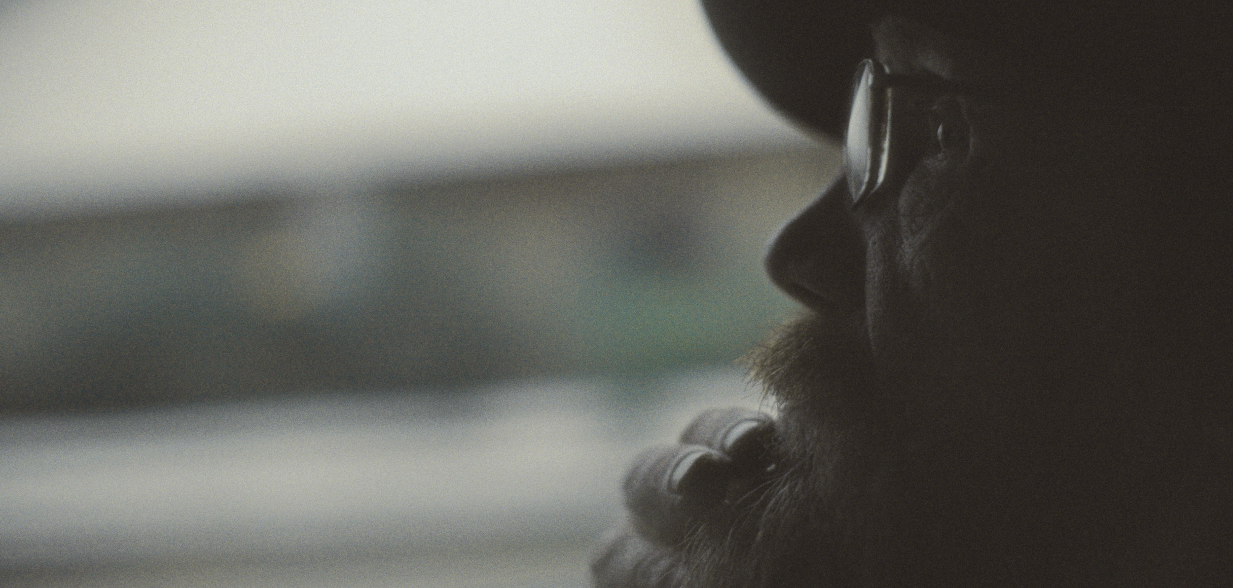 Nærbillede af en persons ansigt i profil, med briller og skæg, i dæmpet lys | Dokumentarfilm | Retrograd | Esben Persson & Anders Mielcke | Filmproduktion Aarhus | GESTALT