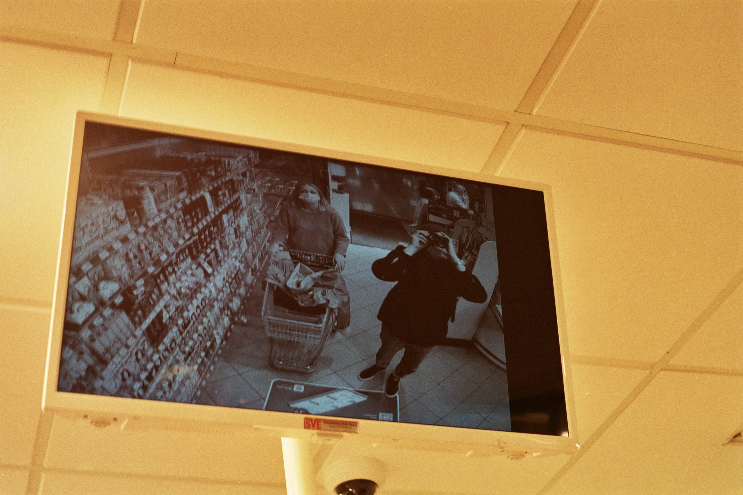 Sikkerhedskamera overvåger butik, med to personer, en kvinde med indkøbsvogn og en mand, der tager billeder | Location scouting Berlin | Kodak | Filmproduktion Aarhus | GESTALT