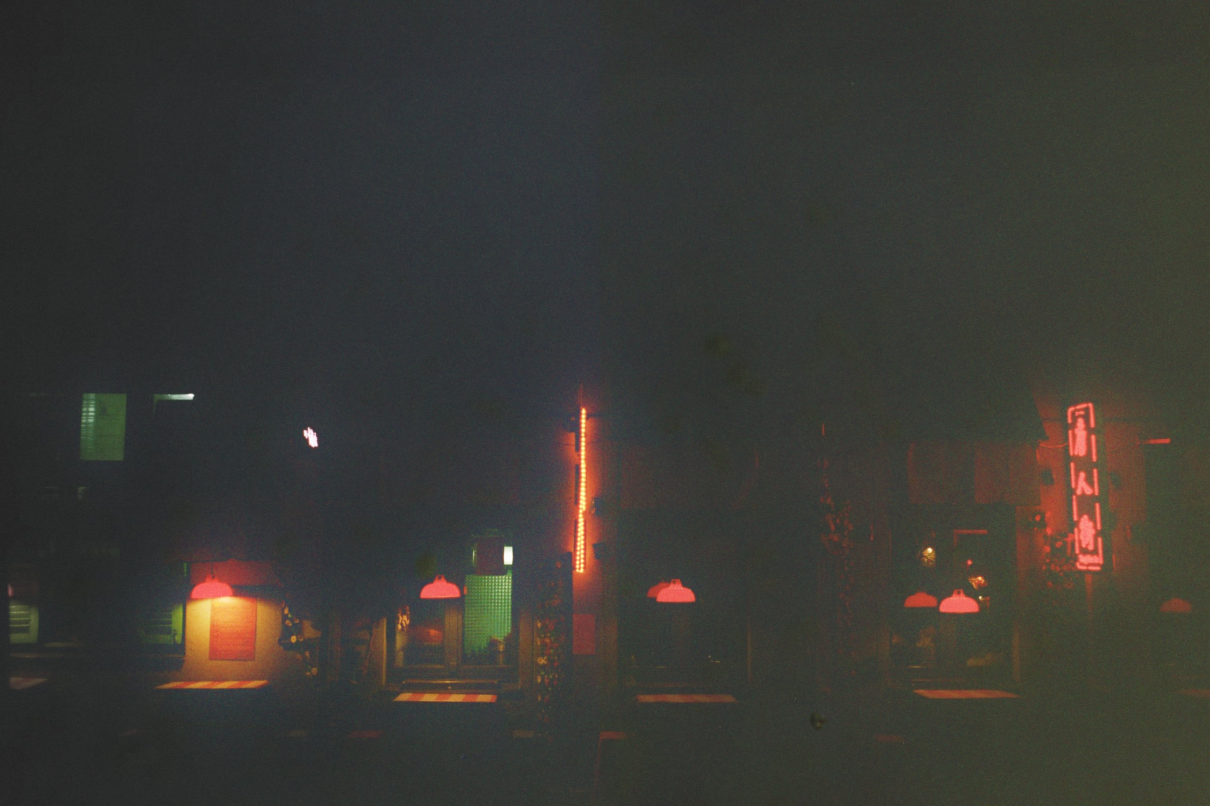 Udsigt mod en mørk gade med neonbelysning, herunder en fjerntliggende neonreklame og flere loftslamper, der lyser svagt op | Location scouting Berlin | Kodak | Filmproduktion Aarhus | GESTALT