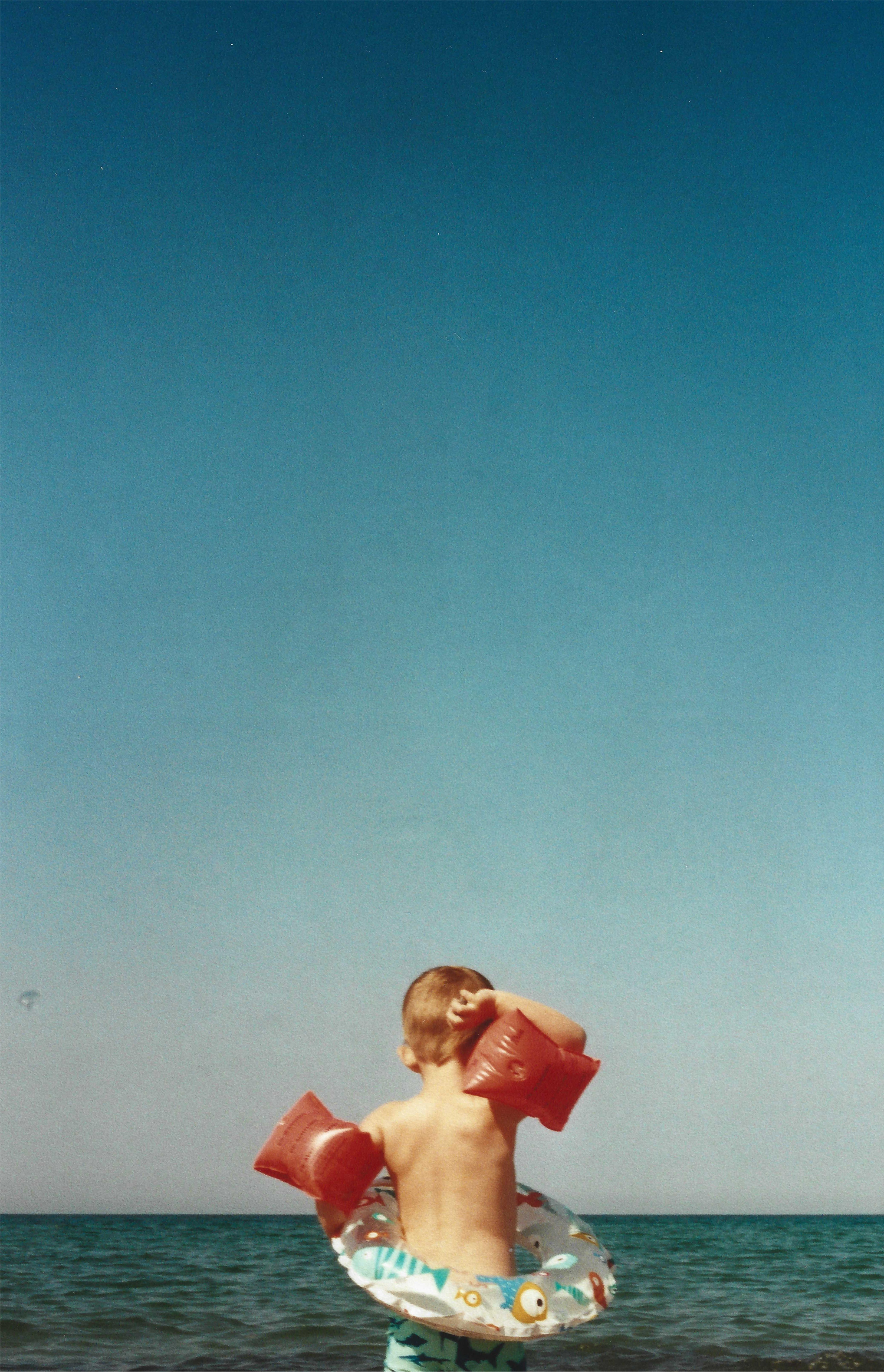 En dreng med badevinger står ved havet med ryggen til kameraet, under en klar blå himmel | Location scouting | Kodak | Filmproduktion Aarhus | GESTALT