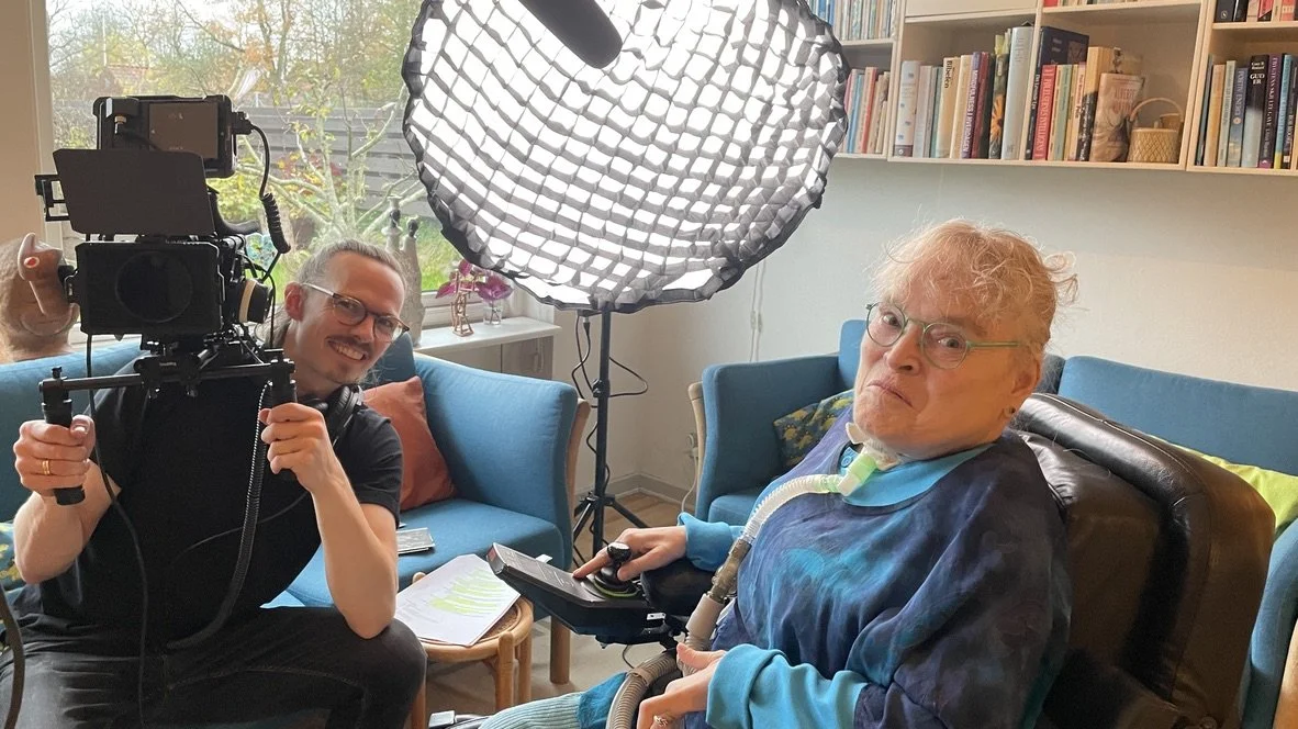 En yngre mand med kamera og headset, der smiler, sidder ved siden af en ældre mand med respirator | Dokumentarfilm | Stemmer fra sær- og åndssvageforsorgen | Anders Mielcke Grønbæk | Filmproduktion Aarhus | GESTALT