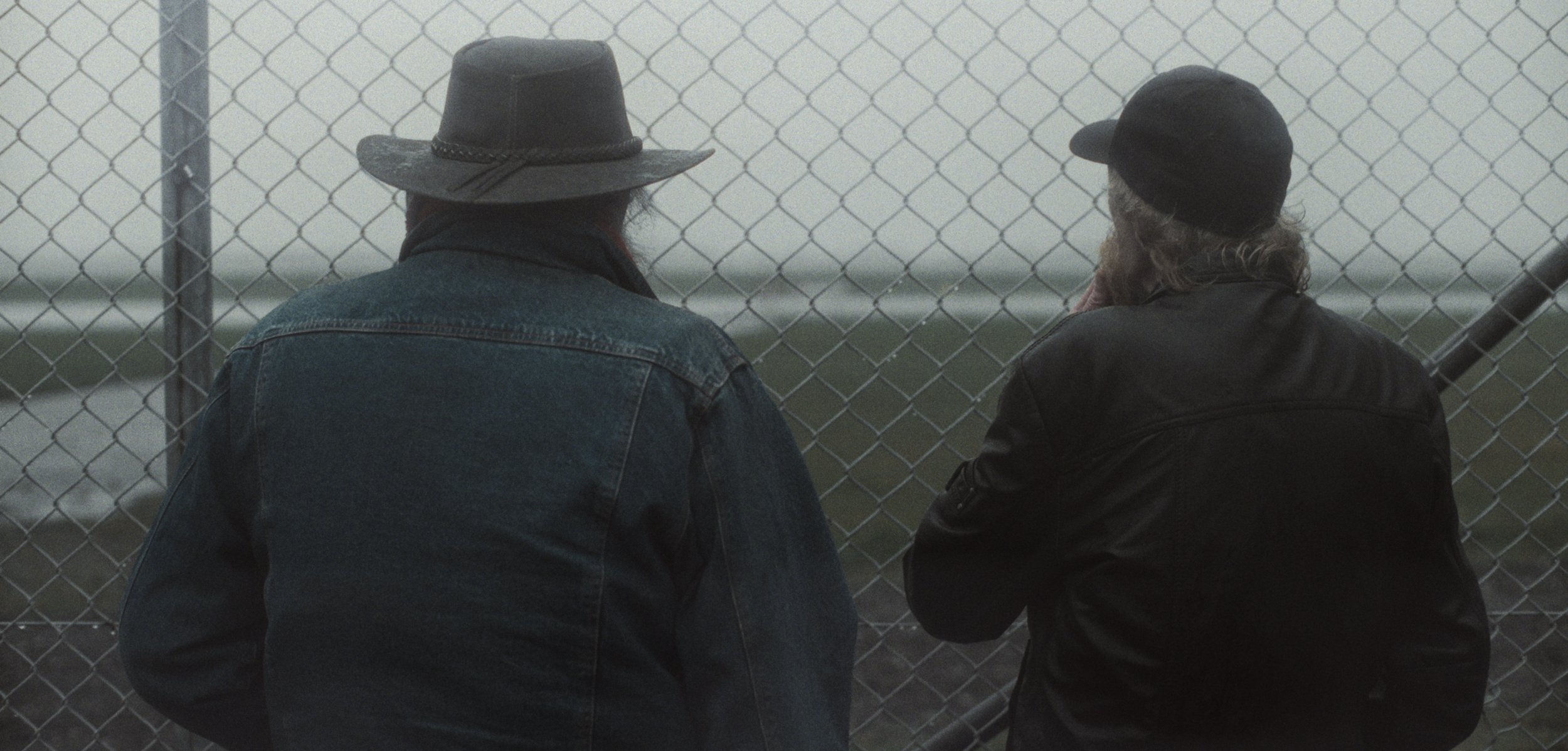 To mænd står foran et hegn i tåge, begge iført jakker og hatte, mens de ser væk | Dokumentarfilm | Retrograd | Esben Persson & Anders Mielcke | Filmproduktion Aarhus | GESTALT