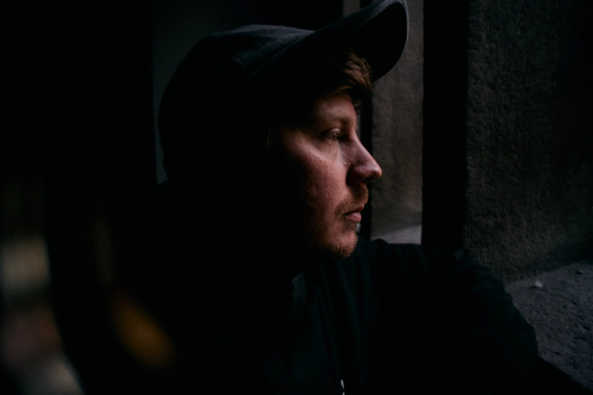 Mand i profil ser ud gennem et vindue i en mørk bygning, med ansigtet næsten i skygge og baggrund af mørke vægge | Dokumentarfilm | Retrograd | Esben Persson & Anders Mielcke | Filmproduktion Aarhus | GESTALT