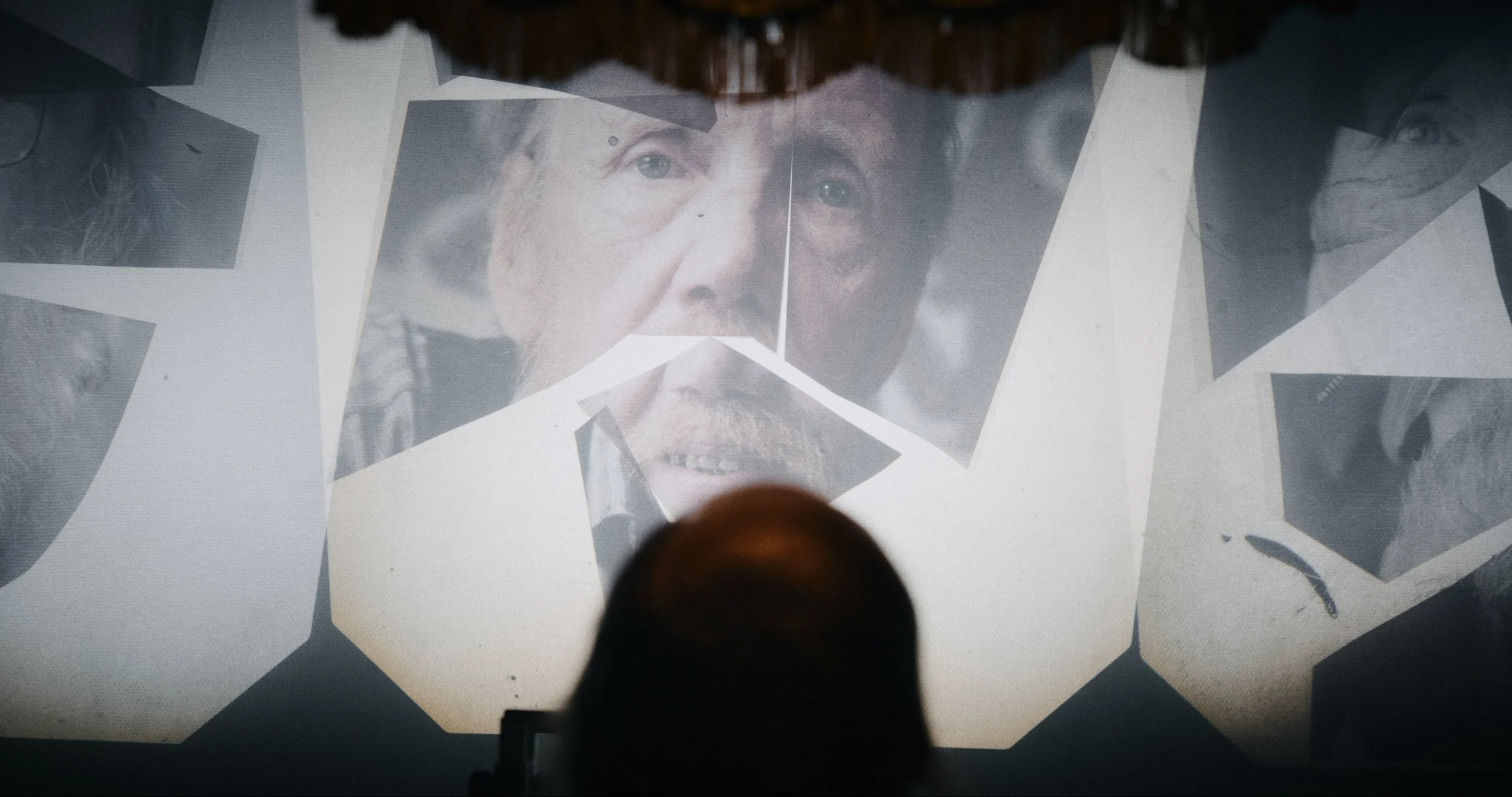 En person kigger op en skærm med flere sammenklippede sort-hvide fotos af menneskehoveder | Dokumentarfilm | Retrograd | Esben Persson & Anders Mielcke | Filmproduktion Aarhus | GESTALT