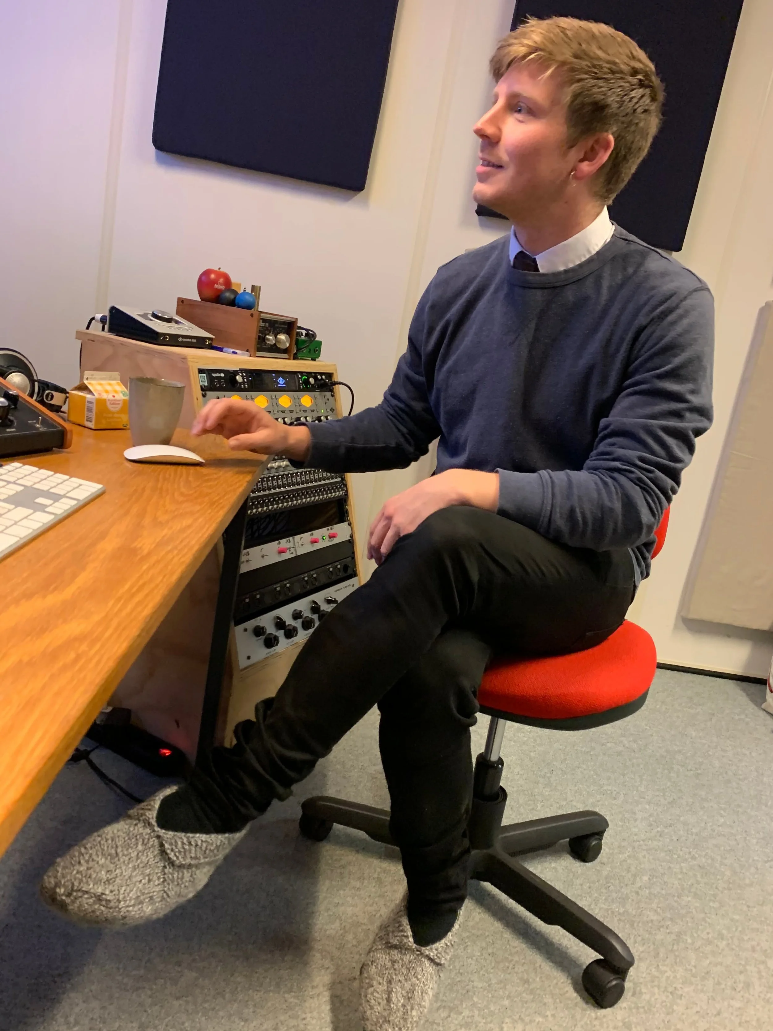 En mand sidder på en kontorstol foran et musik- eller lydudstyr, iført en grå sweater i et lydstudie | Studieproduktion | Musikkomposition | Filmproduktion Aarhus | GESTALT