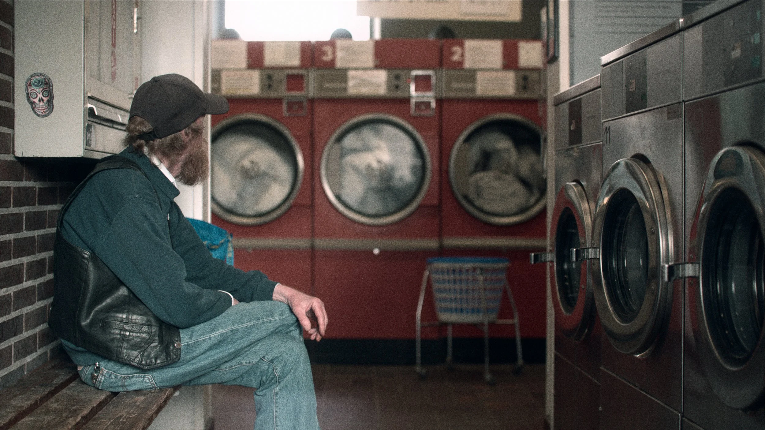 En mand sidder på en bænk med vaskemaskiner i en vaskehal | Dokumentarfilm | Retrograd | Esben Persson & Anders Mielcke | Filmproduktion Aarhus | GESTALT