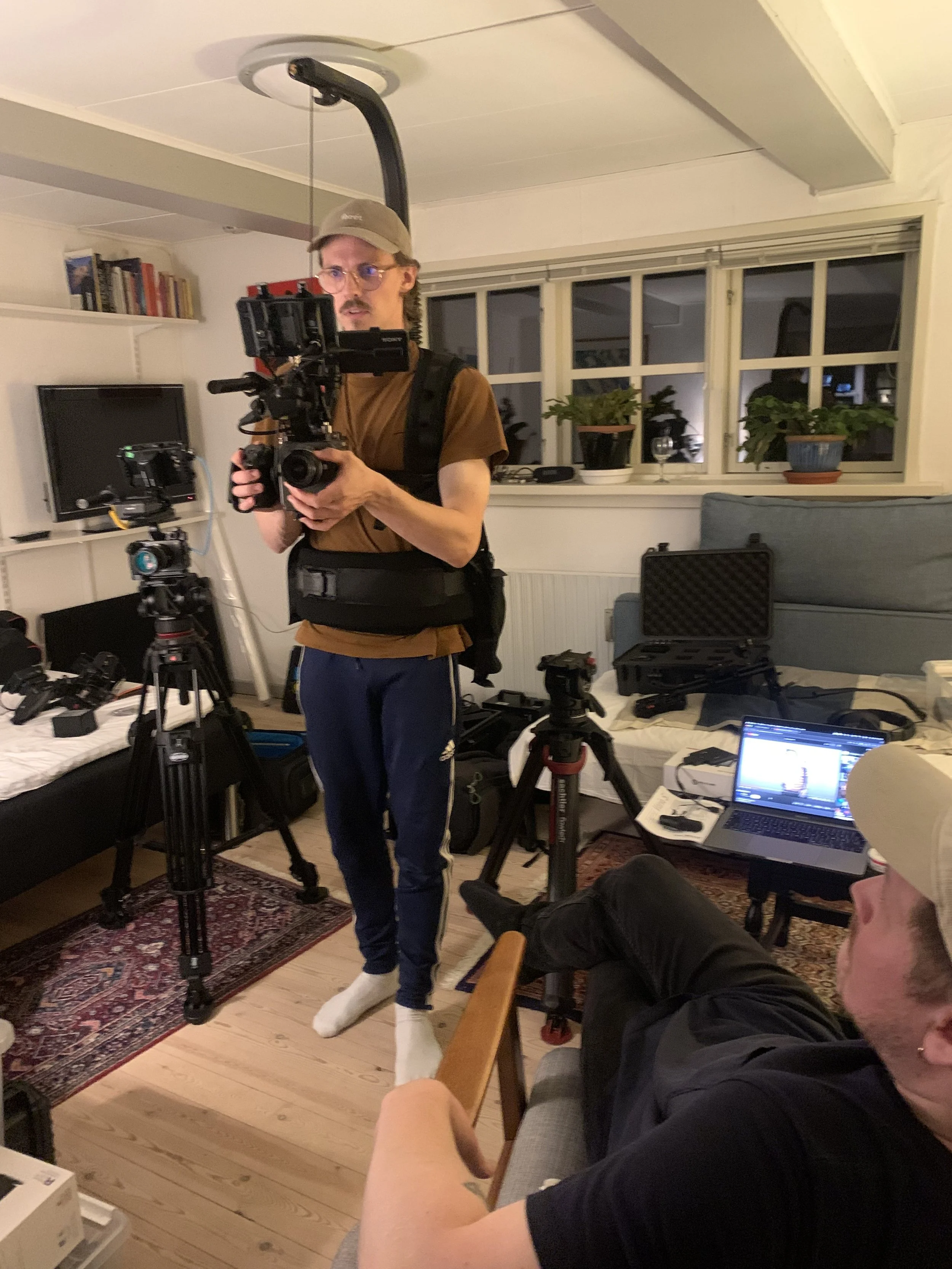 En person står med professionelt kameraudstyr i et hjem, der har sofa, en laptop og kamerastativer | Dokumentarfilm | Retrograd | Esben Persson & Anders Mielcke | Filmproduktion Aarhus | GESTALT