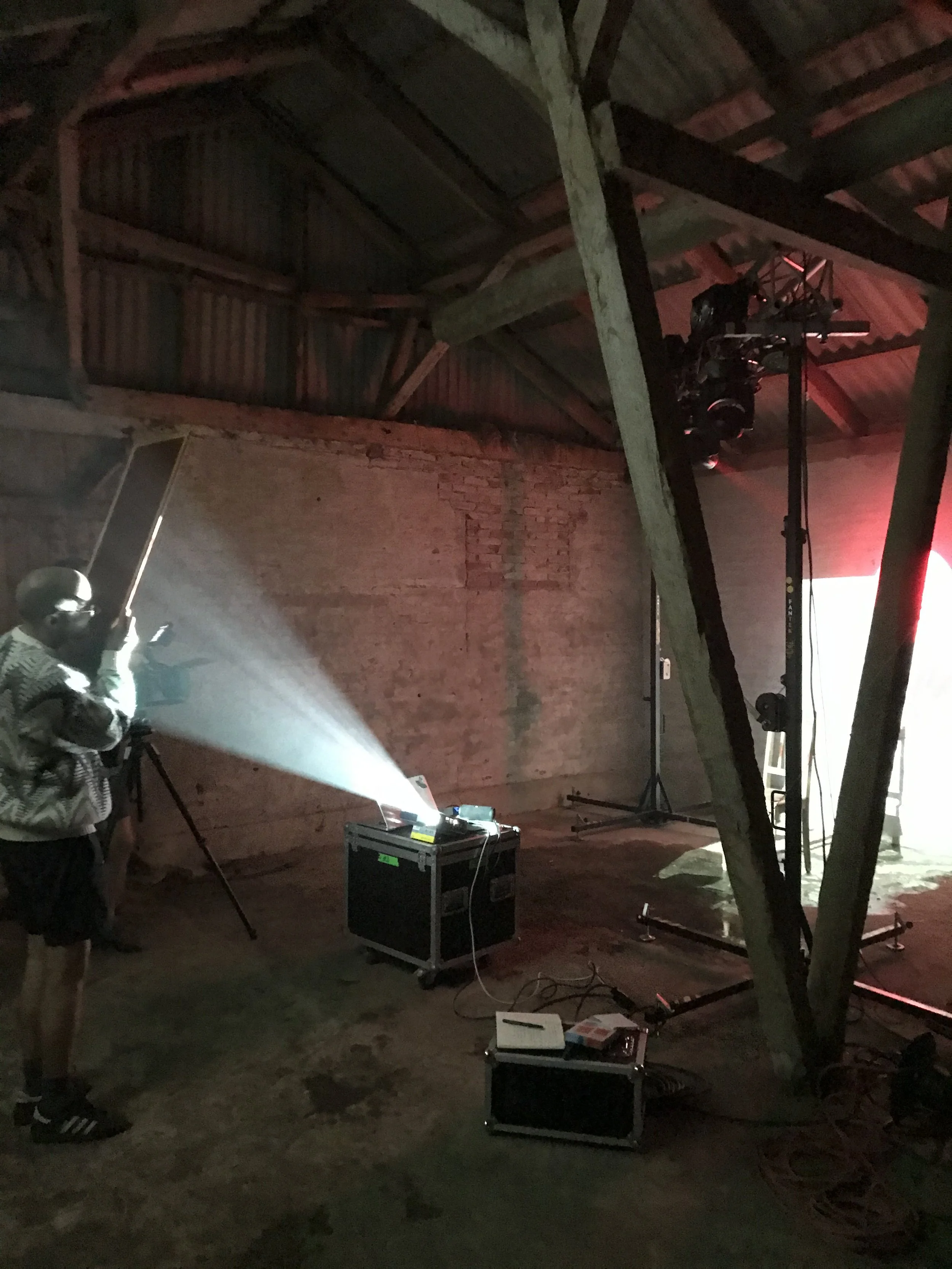 Indendørs foto af en filmsceneopsætning i en gammel, rustik bygning. Der er filmudstyr, herunder et kamera på stativ, en projektor med lys, og kabler på gulvet | Kortfilm | Wild Wild Vesløs | Esben Persson | Filmproduktion Aarhus | GESTALT