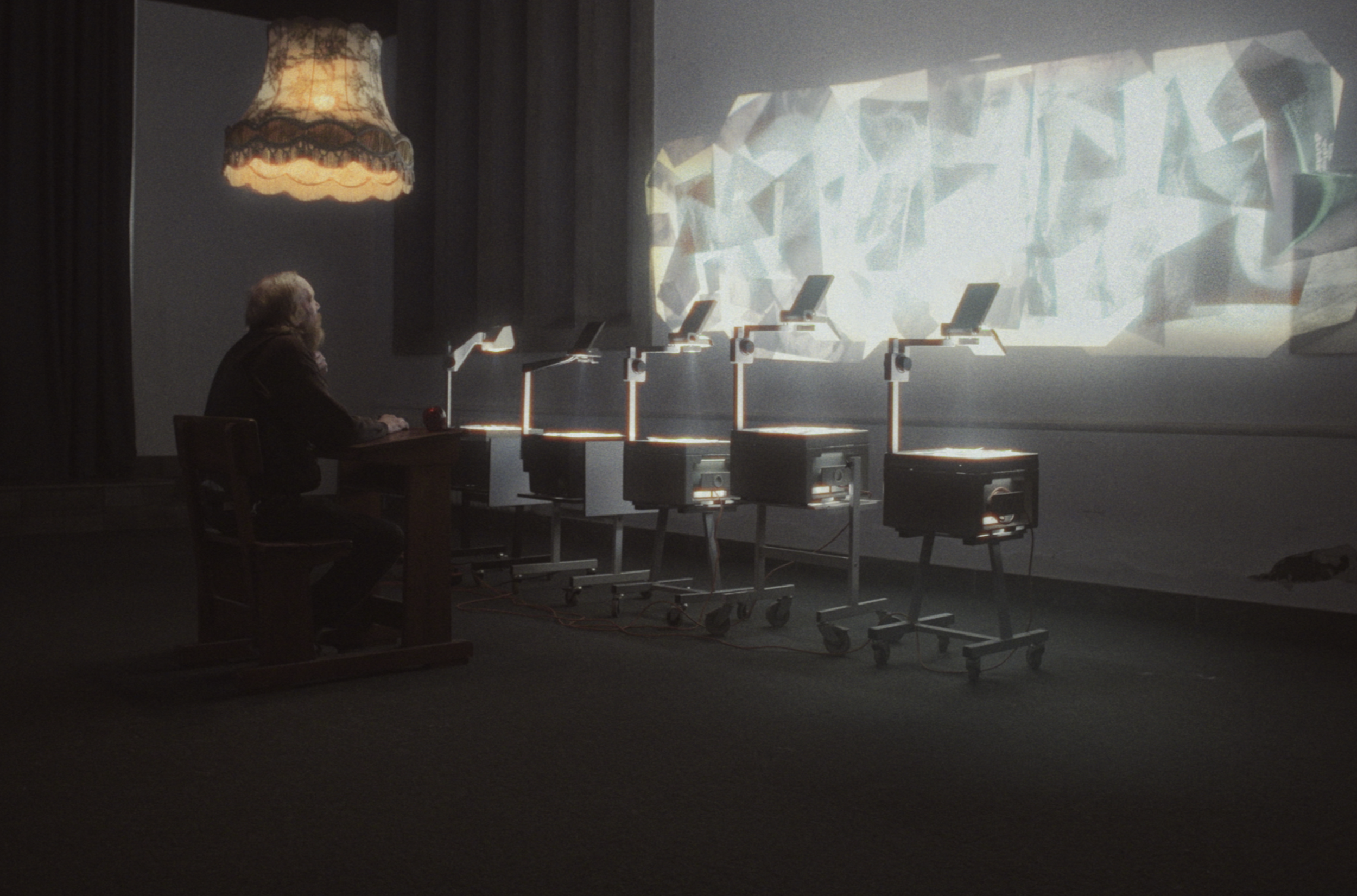 En ældre mand sidder ved et træbord foran fem projektorer | Dokumentarfilm | Retrograd | Esben Persson & Anders Mielcke | Filmproduktion Aarhus | GESTALT