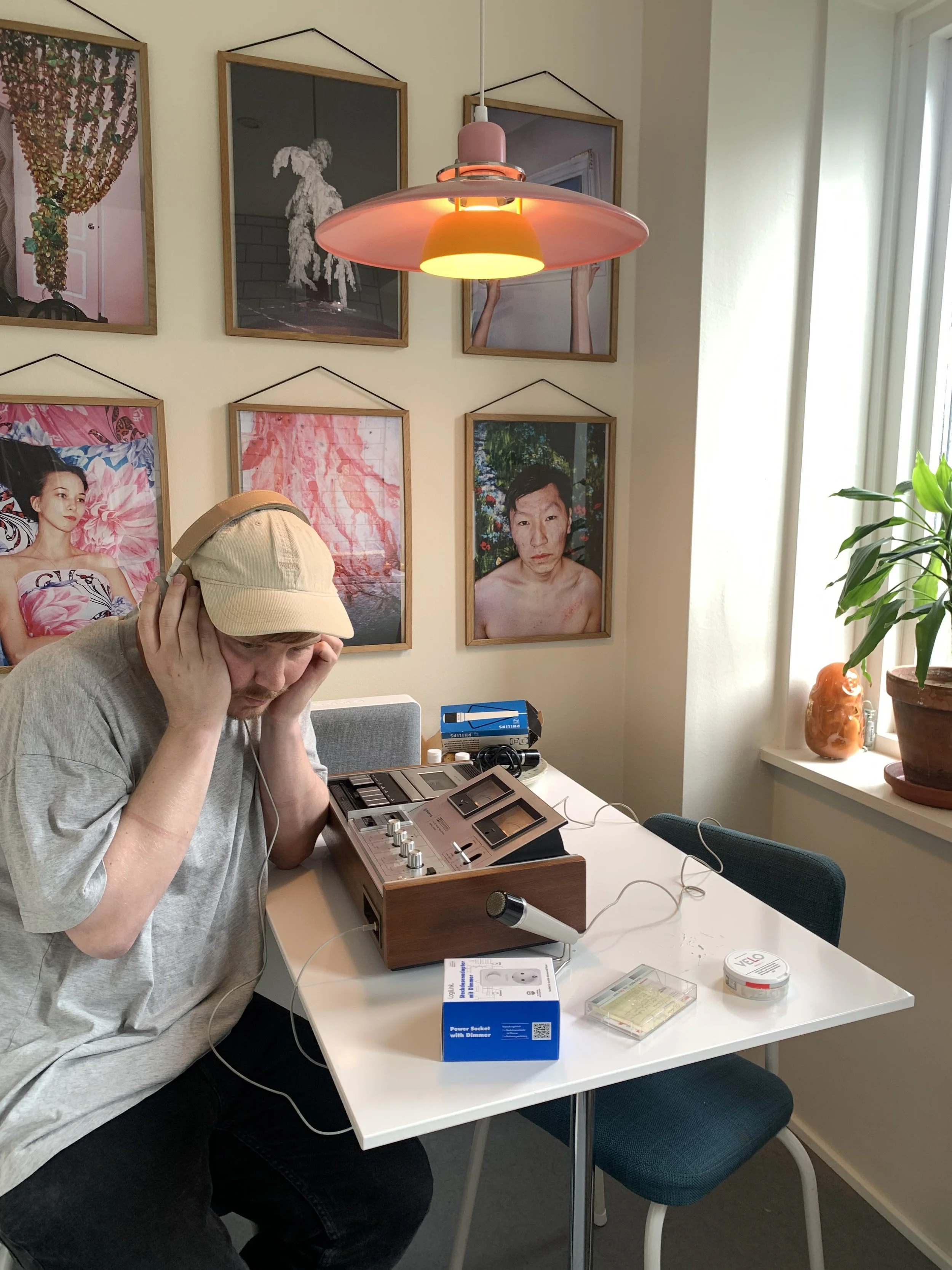 Person med beige hat lytter til musik på gammel båndoptager med høretelefoner i et rum med billeder på væggen | Musikkomposition | Lyddesign  | Filmproduktion Aarhus | GESTALT