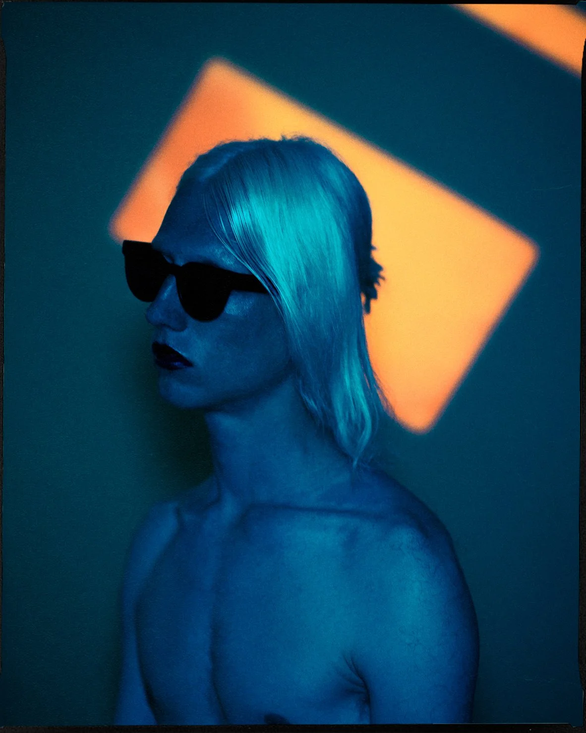 Portræt af en mand med blond hår, peger i blå og orange belysning, bruger sorte solbriller | Testoptagelser | Filmproduktion i Aarhus | GESTALT