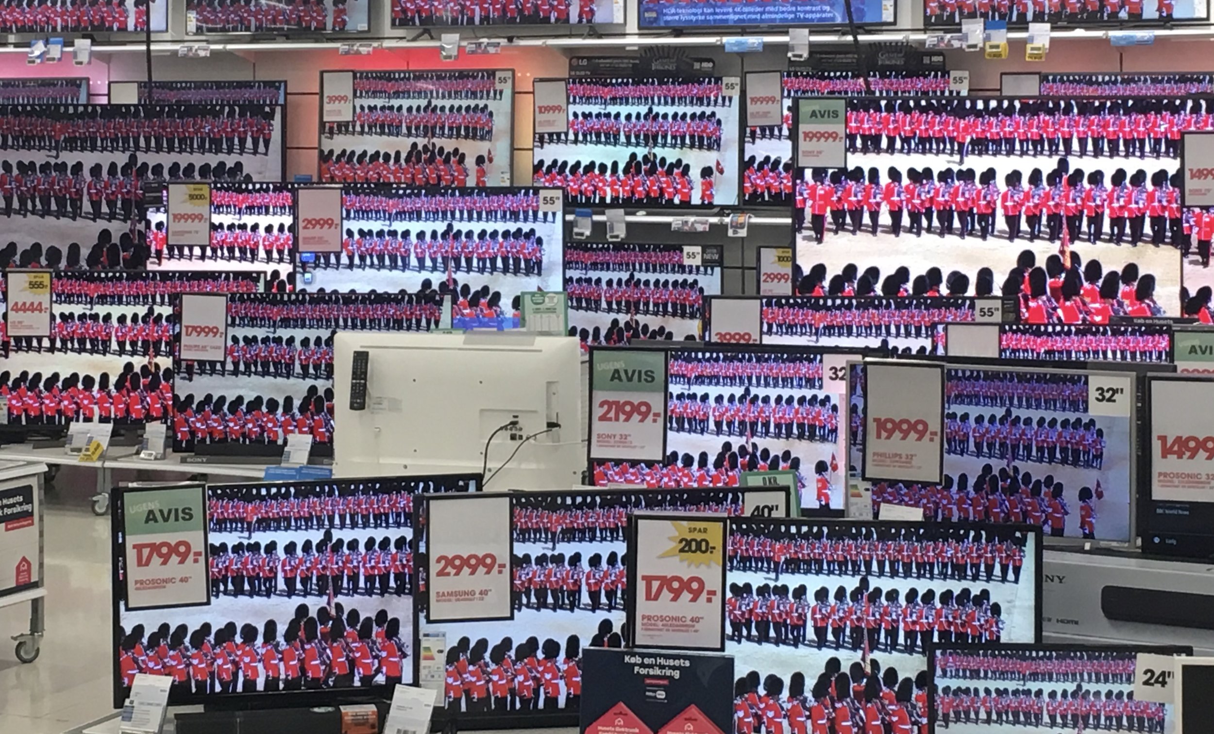 Flere tv-skærme i en butik med billeder fra Den Kongelige Livgarde, viser nøjagtigt de samme soldater i uniforme, arrangeret i rækker og kolonner | Location scouting | Filmproduktion i Aarhus | GESTALT