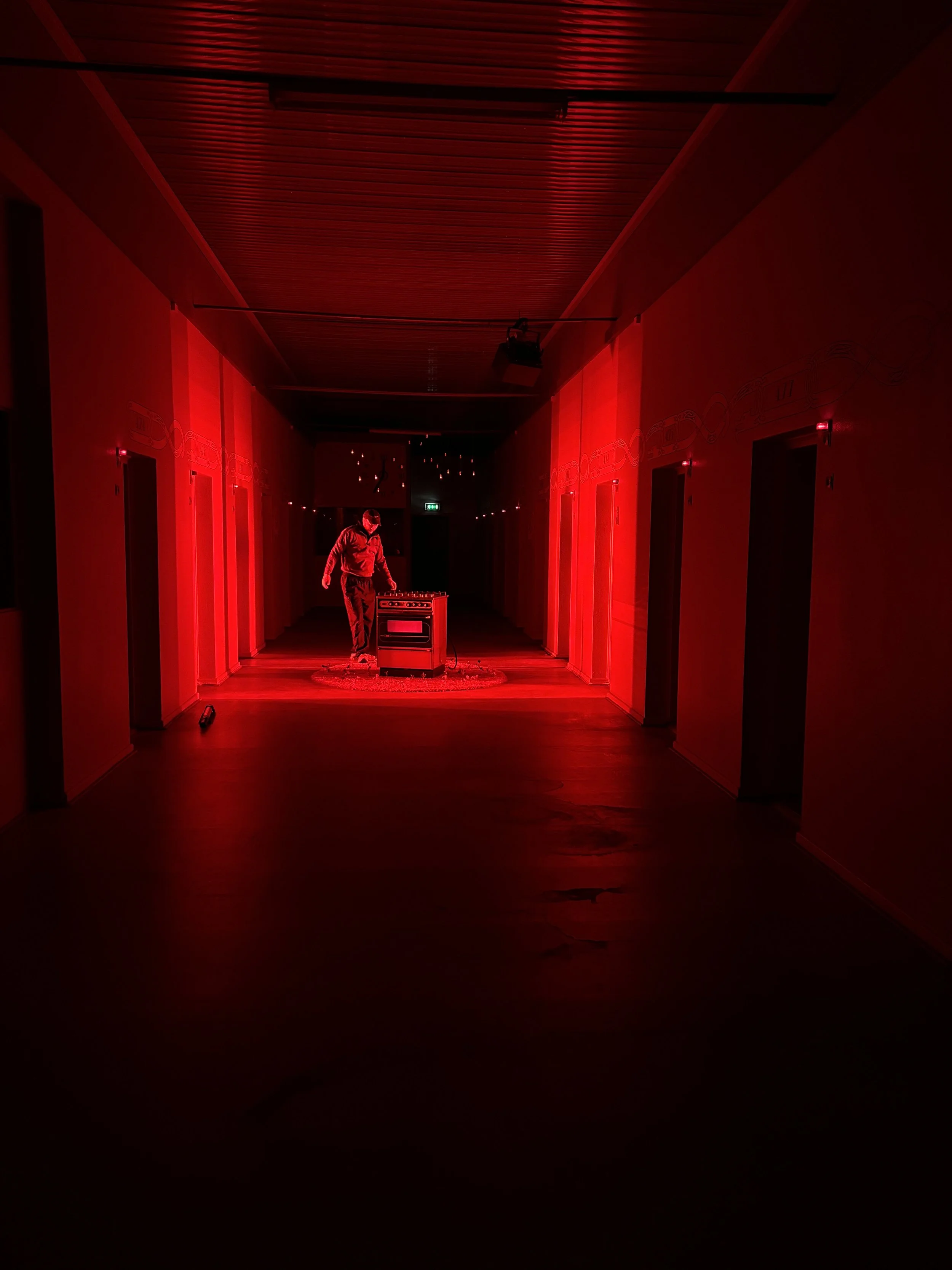 En person står foran en retro gasovn i en mørk korridor, badet i rødt lys | Dokumentarfilm | Retrograd | Esben Persson & Anders Mielcke | Filmproduktion Aarhus | GESTALT