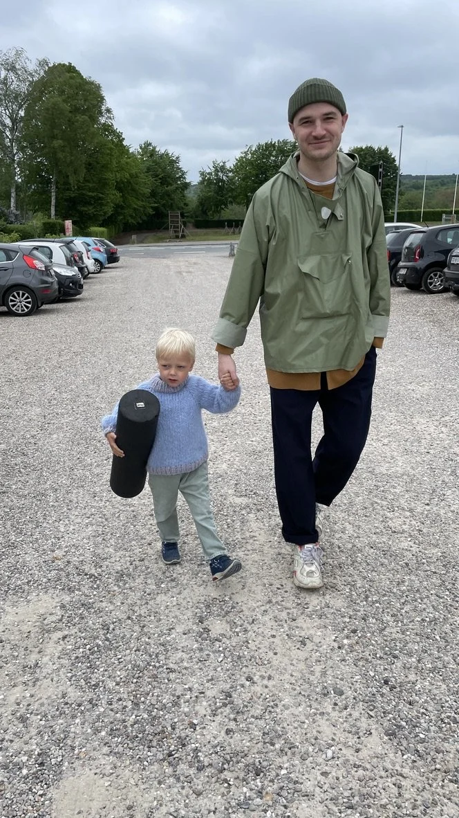 En voksen mand og et lille drengen går hånd i hånd, på en parkeringsplads med biler | Bagom billeder | Filmproduktion i Aarhus | GESTALT 