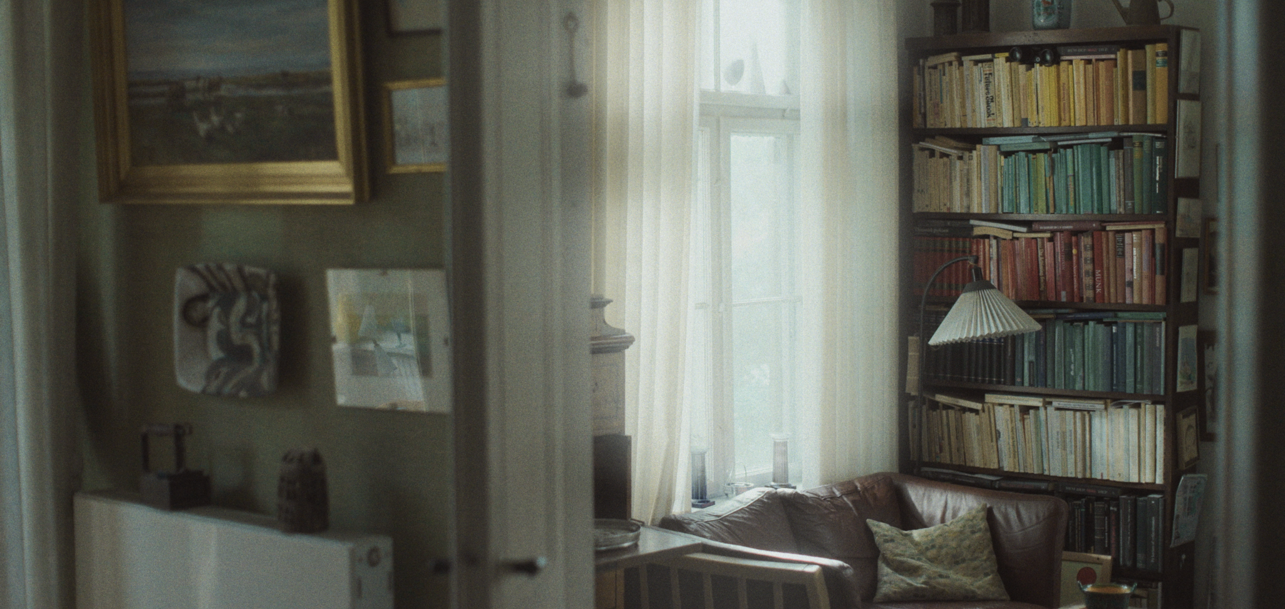 Et hyggeligt opholdsrum med en brun lædersofa, en væg fuld af bøger, og et lille læselampe | Dokumentarfilm | Retrograd | Esben Persson & Anders Mielcke | Filmproduktion Aarhus | GESTALT