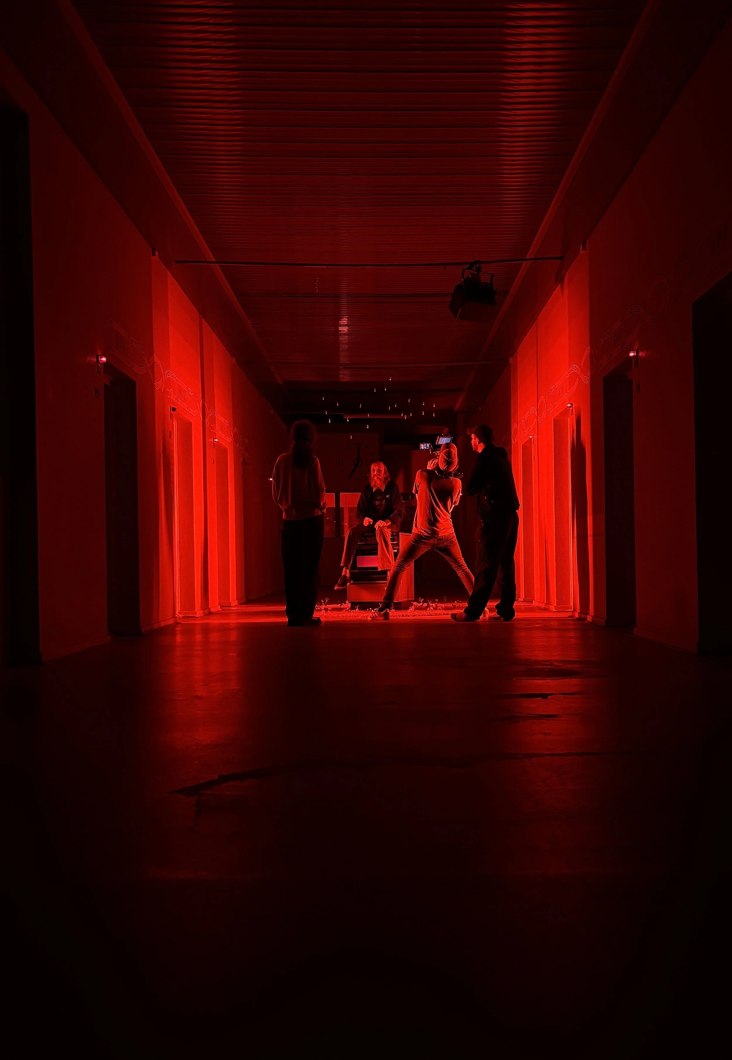 En mørk korridor med rødt lys, hvor en person sidder på en gammel gasovn. Der er filmudstyr, herunder et kamera, rettet mod personen på scenen. | Dokumentarfilm | Retrograd | Esben Persson & Anders Mielcke | Filmproduktion Aarhus | GESTALT