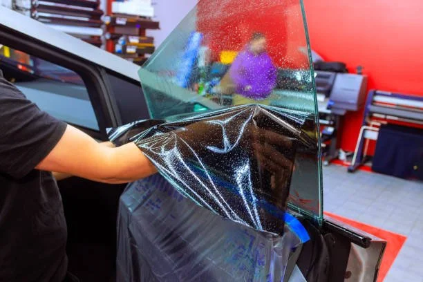 Professional car window tint installation with a technician applying tint film to a vehicle window.