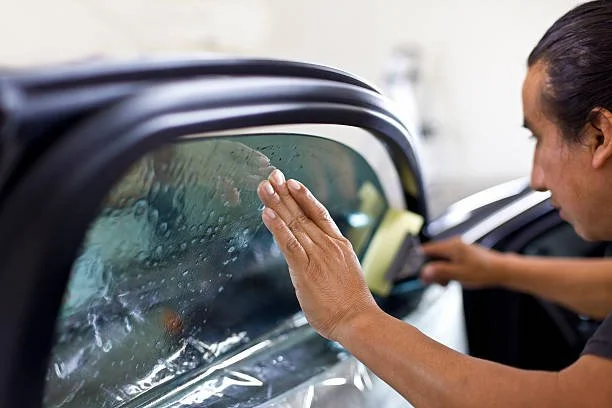 Professional window tint installer applying film to a car window during installation.