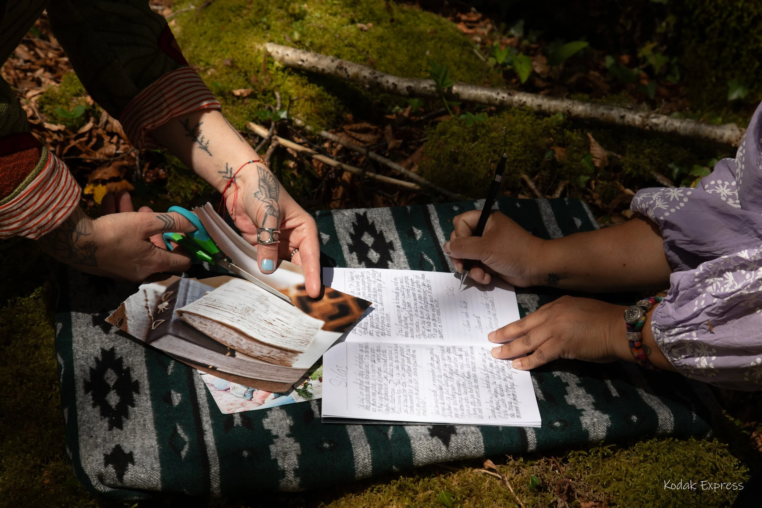 Deux personnes écrivent et prennent des notes lors d'une activité en plein air, avec un livre ouvert, des feuilles de papier et des stylos posés sur une couverture en tissu avec un motif géométrique.