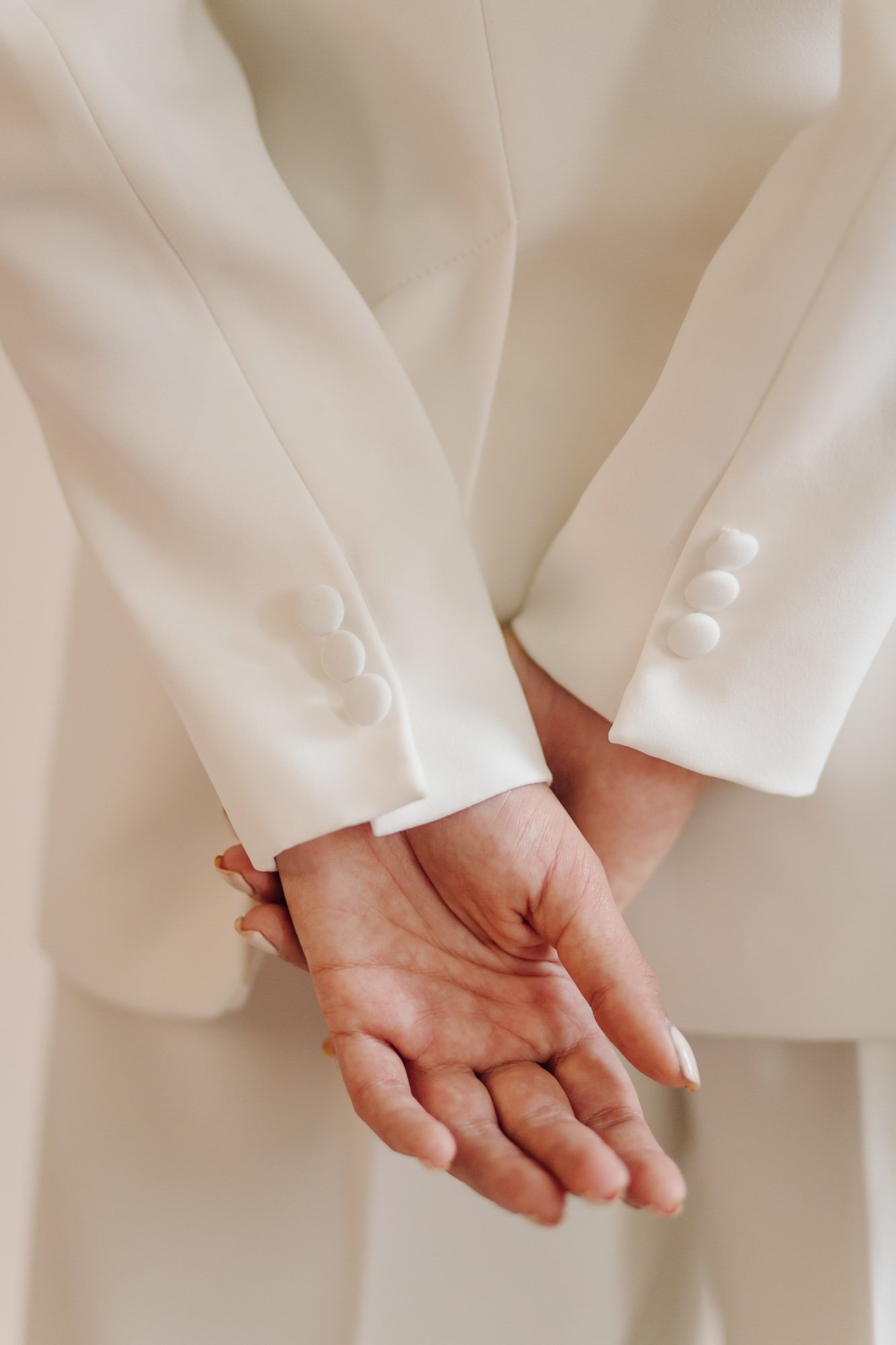 Close-up of a person in an elegant white blazer with button details, holding hands behind their back.