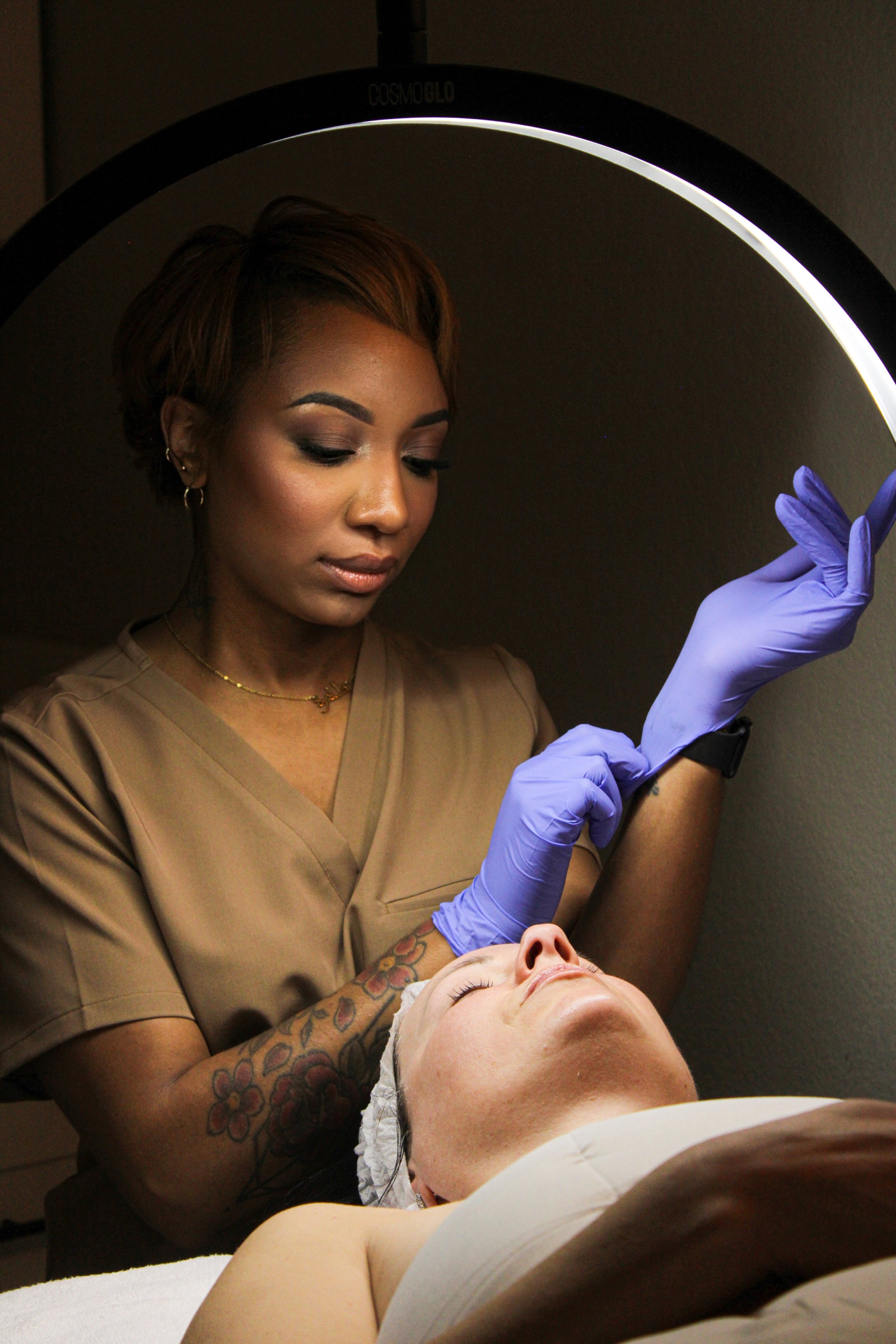 Esthetician giving facial treatment to a client under a magnifying lamp.