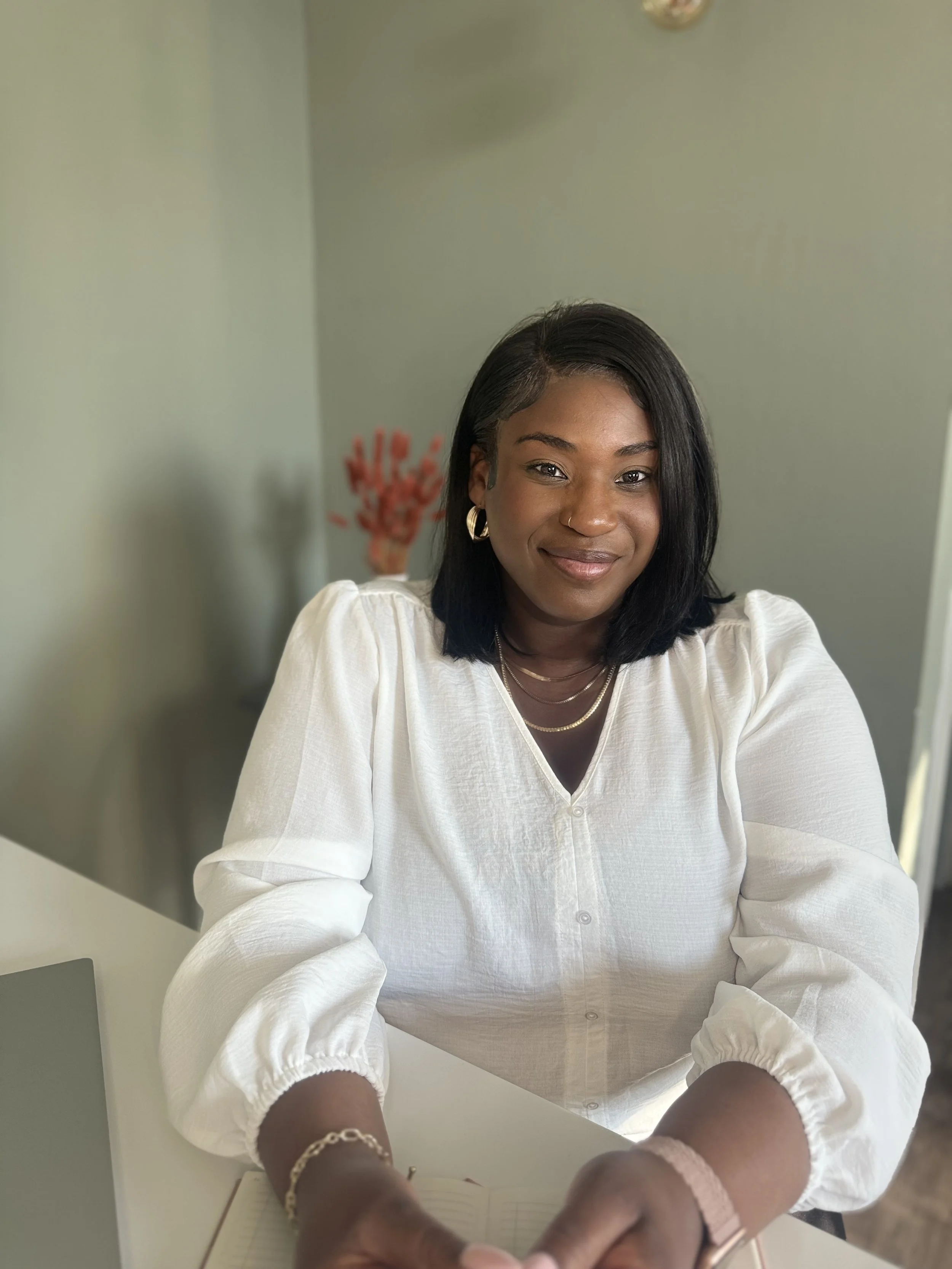 Bonita Carmel seated at her desk, smiling gently—sharing her journey from personal challenges to purpose-led coaching that empowers ambitious women to embrace their worth.