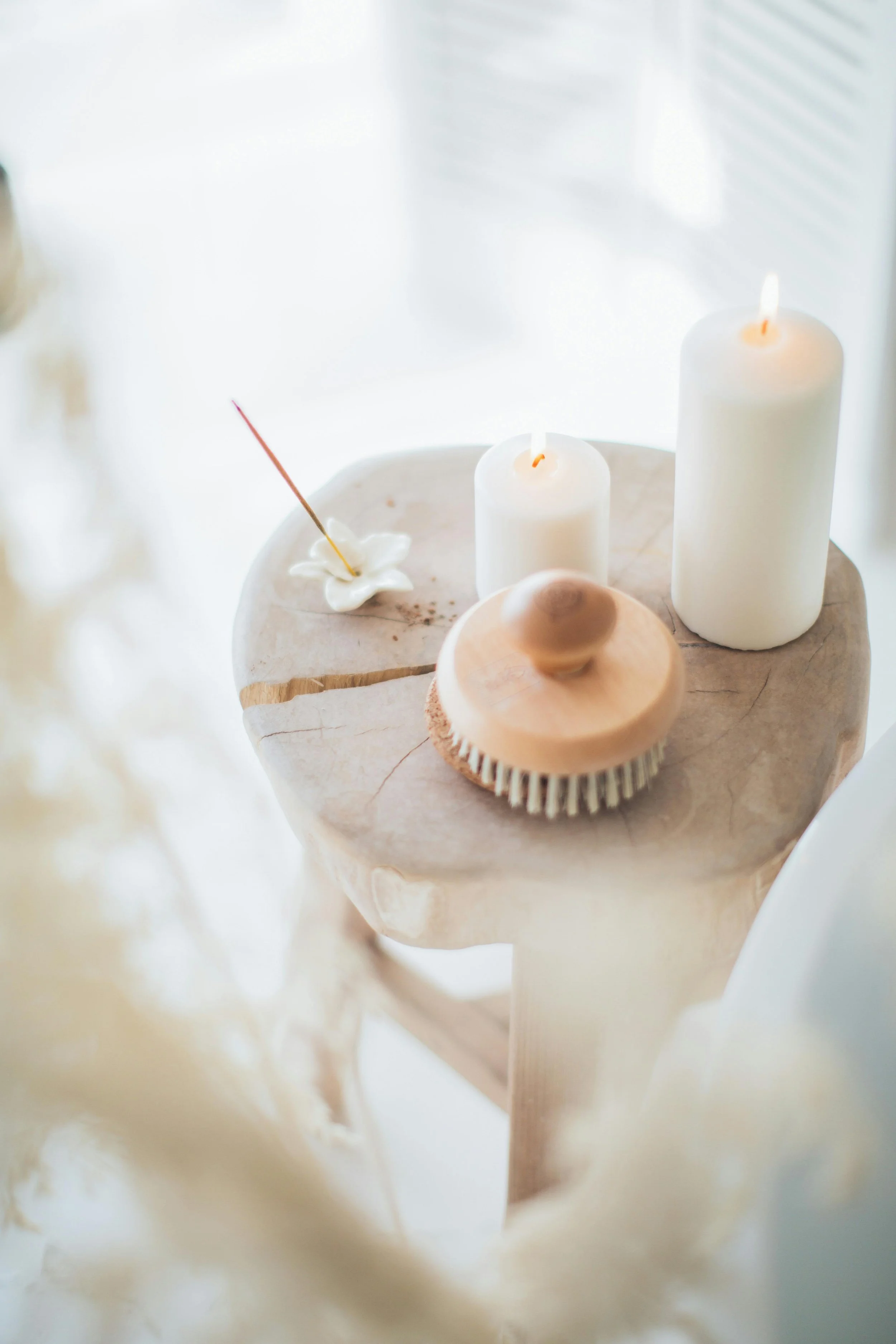 A calming scene with lit candles, a body brush, and incense on a wooden stool—symbolising Bonita Carmel’s holistic coaching approach that nurtures self-care, balance, and inner peace.