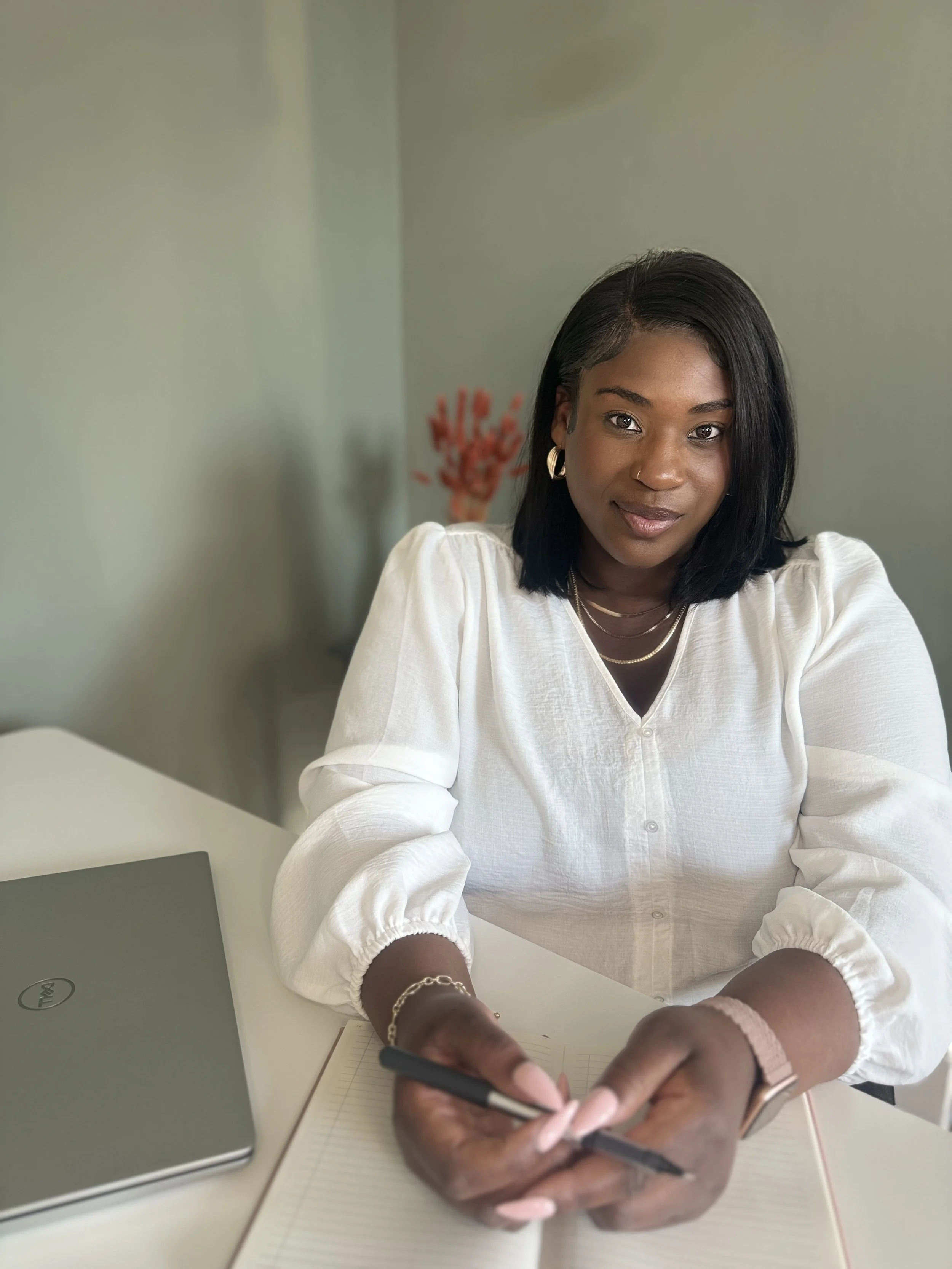 Bonita Carmel sitting with a pen in hand and an open notebook—offering a calm, grounded presence that reflects the importance of choosing a coach who truly sees and supports your self-acceptance journey.