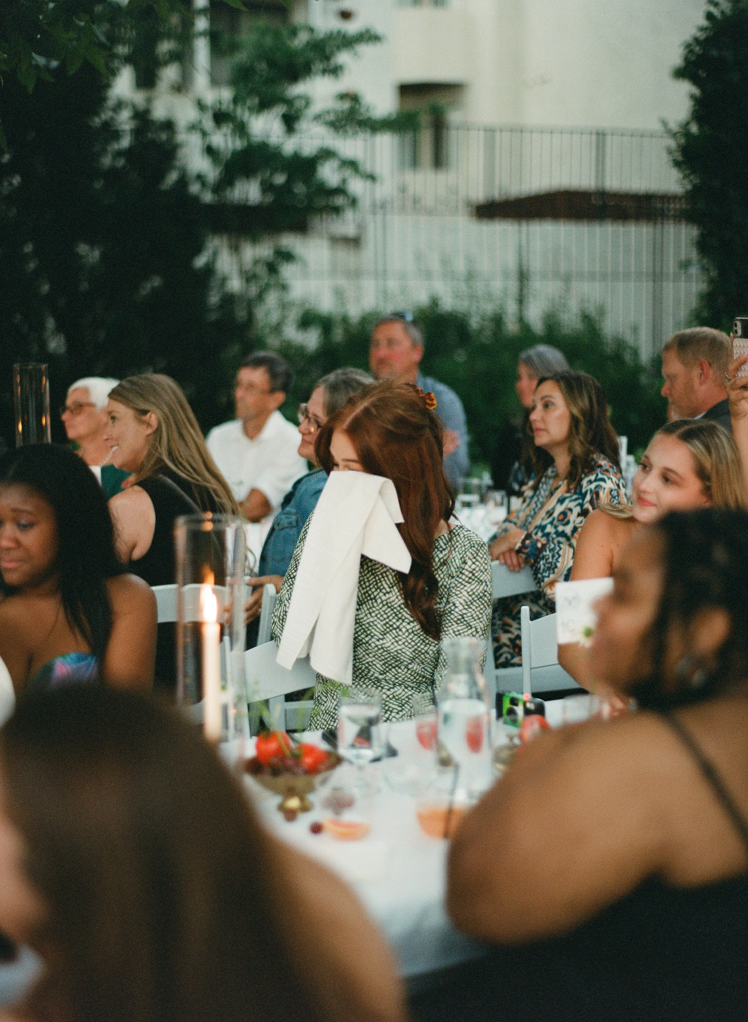People seated at an outdoor wedding. One person wipes a tear with a napkin.