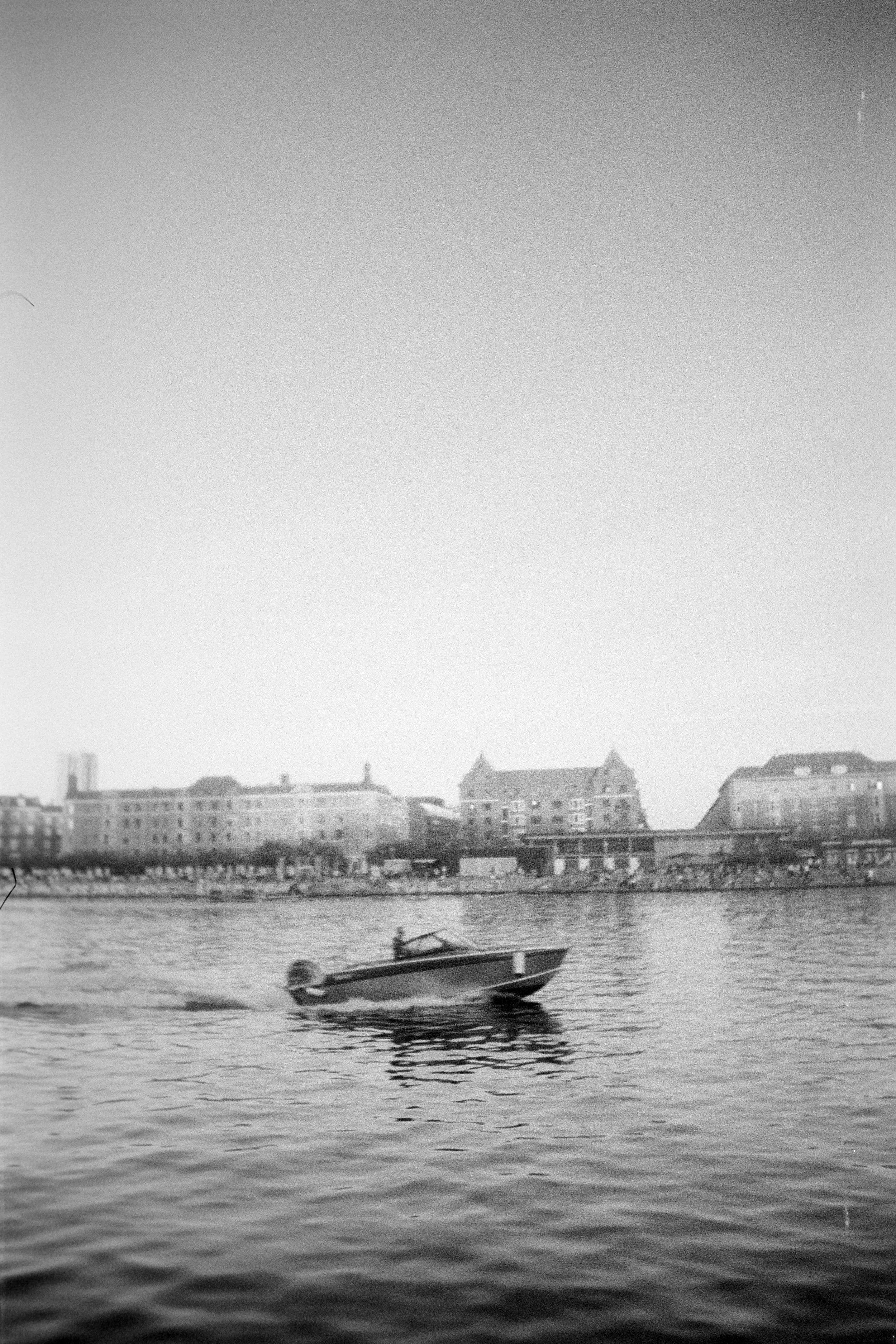 A small motorboat cruising on a river with a cityscape in the background.