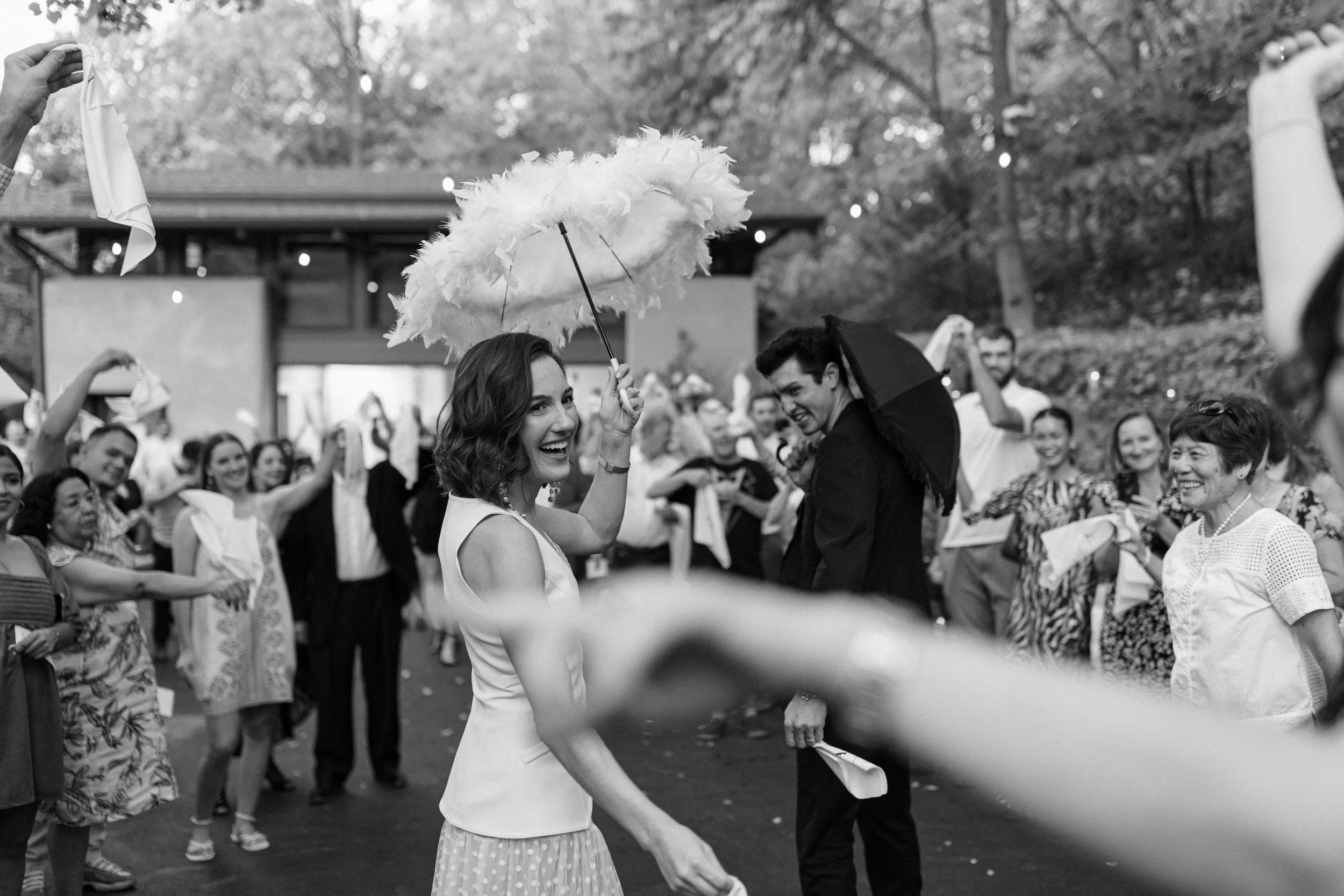 A couple during a second line dance holding their umbrellas and walking through the crowd of their loving friends and family.