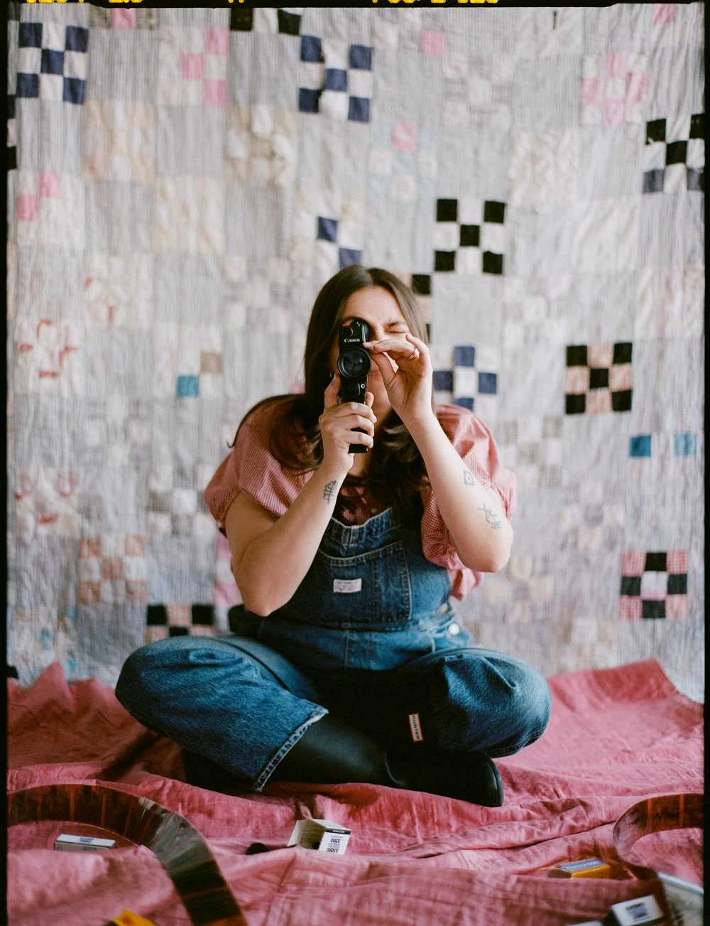 Delaney Hady sitting cross-legged on a pink quilted blanket, with a SUper 8 camera, with a quilt hanging in the background.