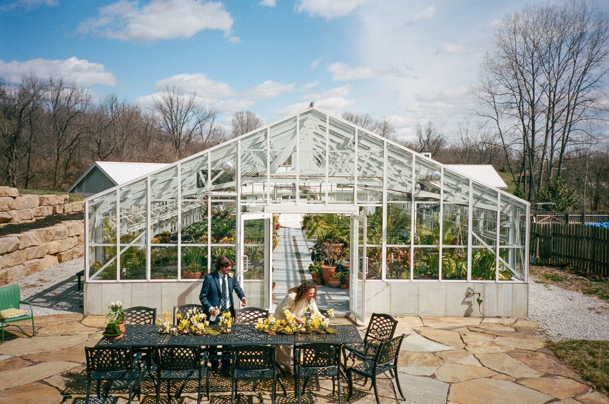 Photo of a couple outside a green house setting up their tables for their cake cutting and after party.