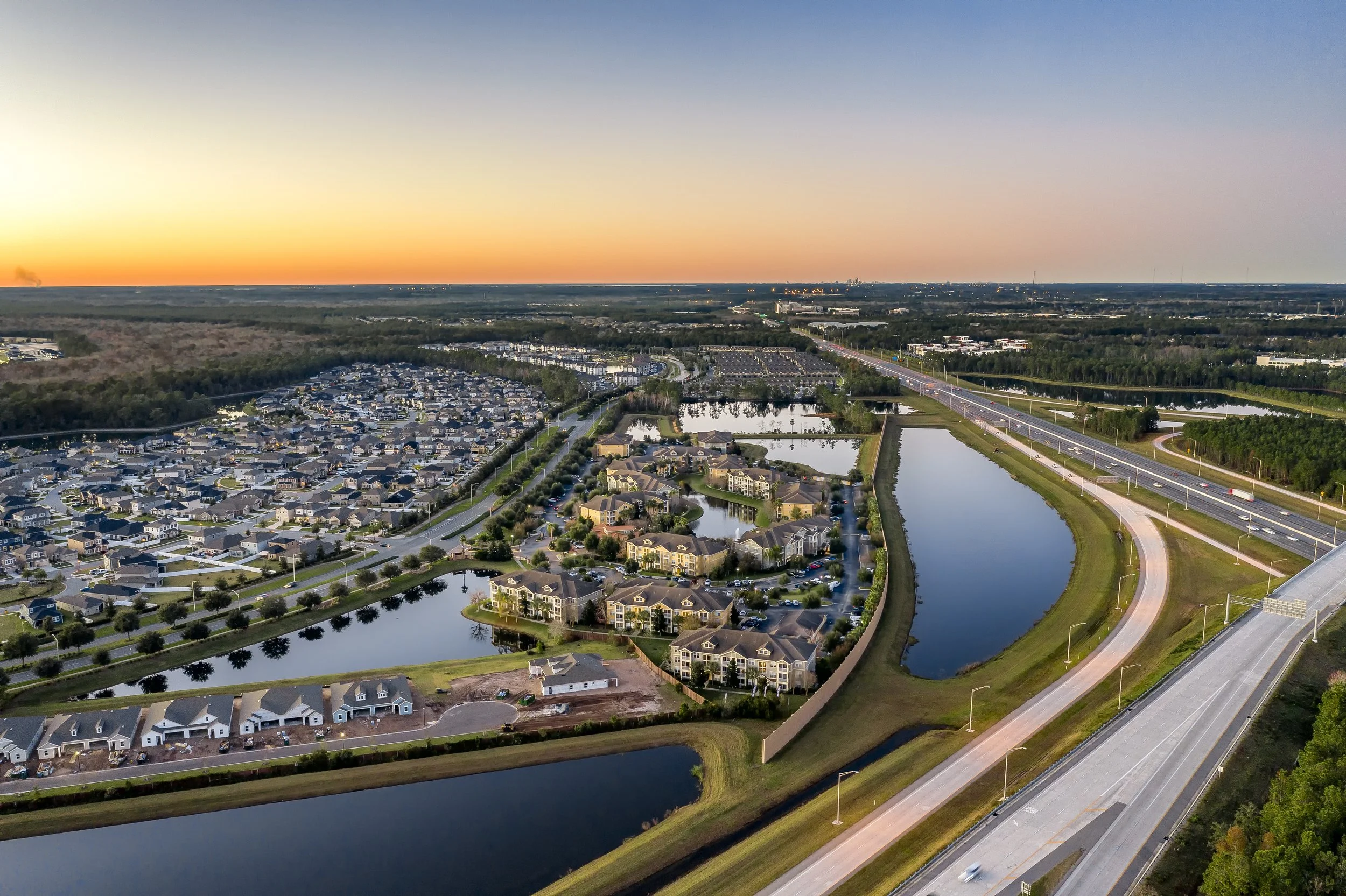 Aerial view of the Bartram Park neighborhood with houses, roads, and ponds, next to a major highway at sunset.