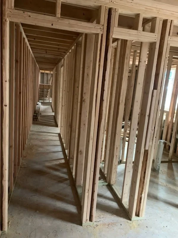 Wooden framing inside a building under construction, featuring exposed beams, studs, and an unfinished hallway.