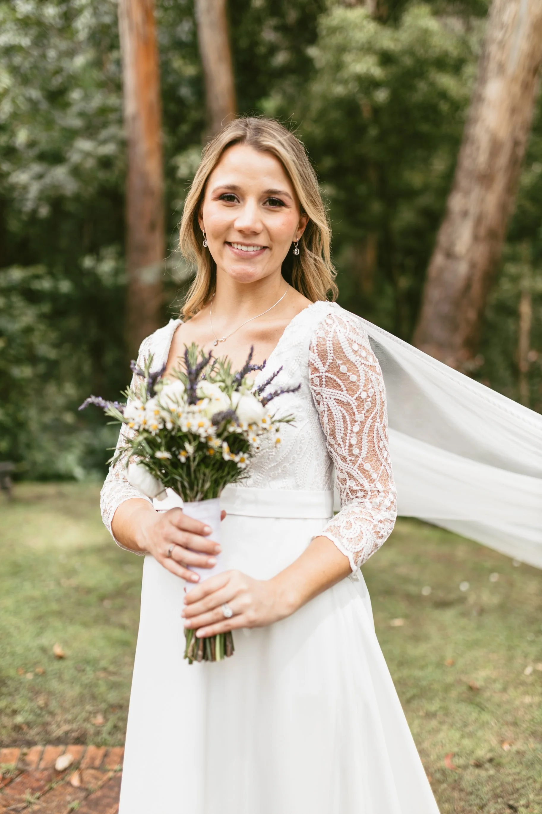 Mujer con vestido de novia sosteniendo ramo de flores en un entorno natural con árboles.
