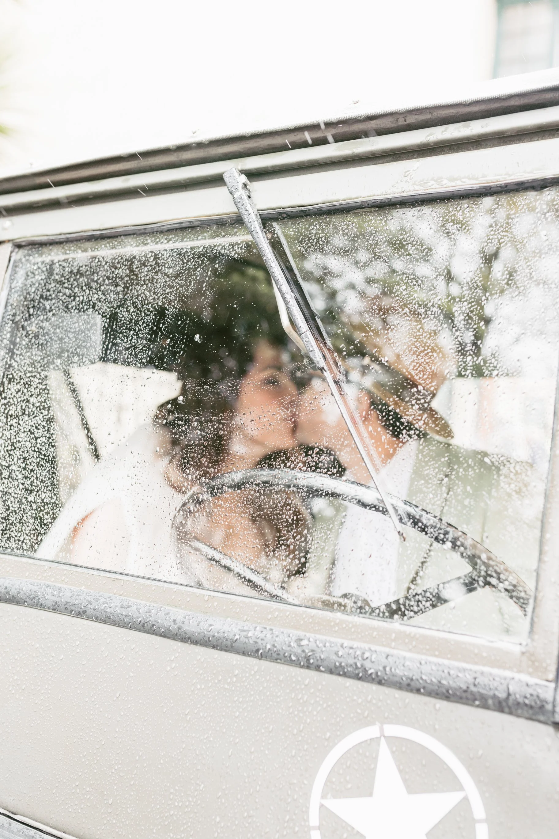 Dos personas en un vehículo antiguo, visto a través de una ventana con gotas de lluvia, uno manchando y el otro con sombrero.