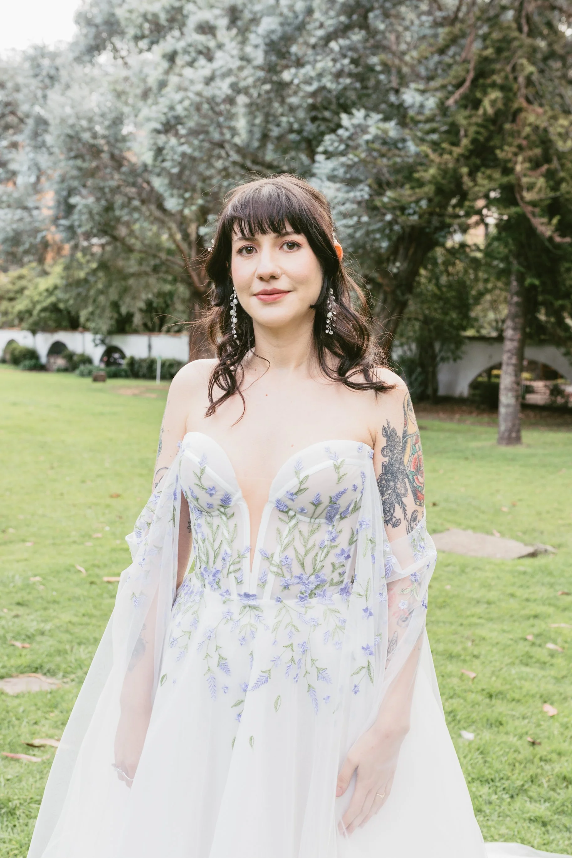 Mujer con vestido de novia en un parque con árboles y césped verde.